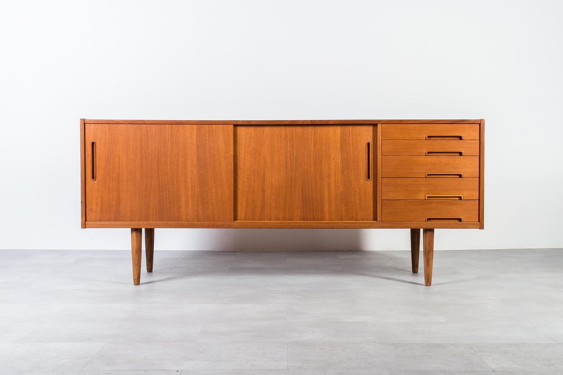 Discover the exquisite craftsmanship of this unique Nils Jonsson teakwood sideboard, boasting a distinctive Scandinavian Modern style. Crafted with precision and elegance, it features two sliding doors, adorned with two sculpted handles and a