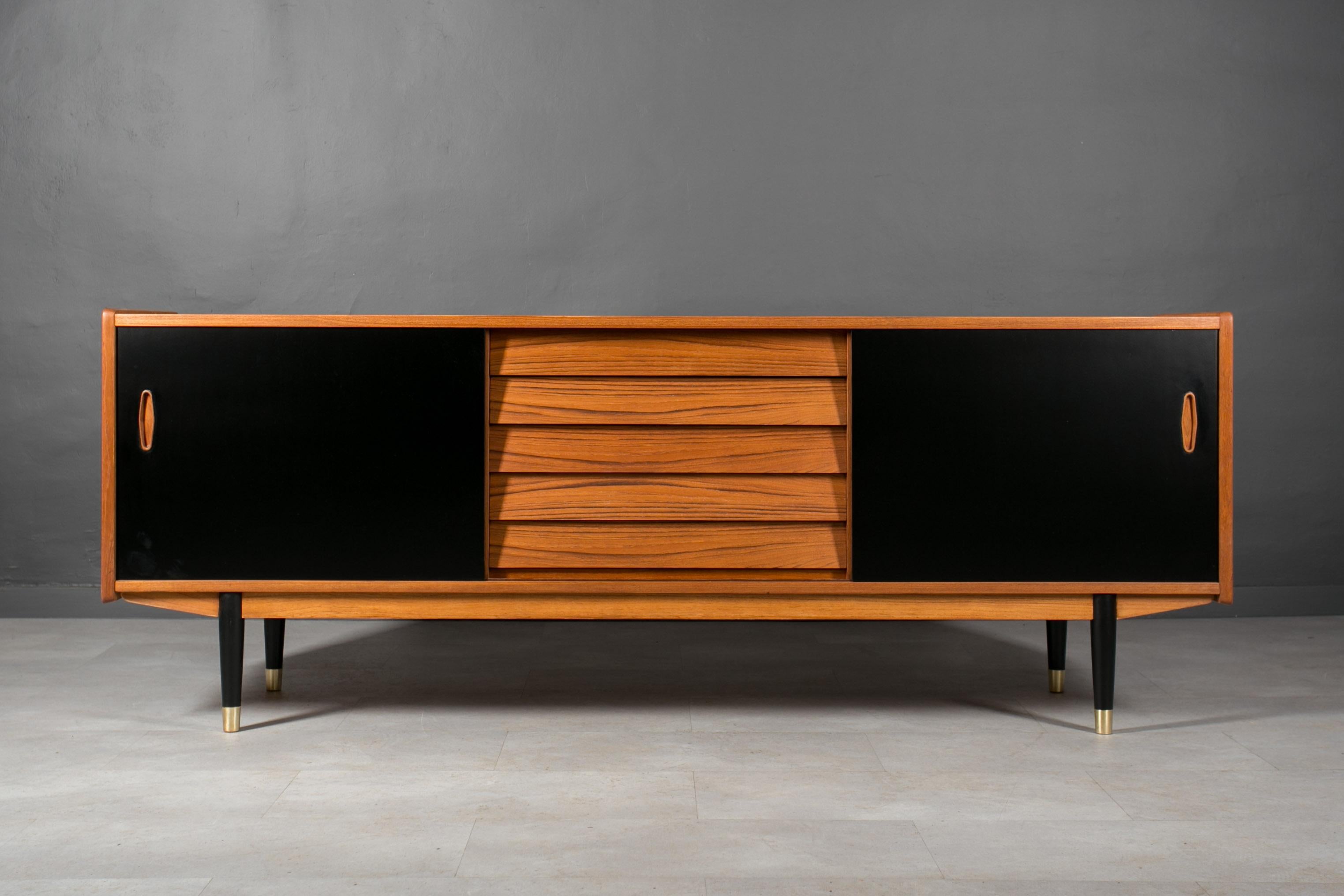 Discover the exquisite craftsmanship of this unique Nils Jonsson teakwood sideboard, boasting a distinctive Scandinavian Modern style. Crafted with precision and elegance, it features sleek black sliding doors adorned with two sculpted handles and a