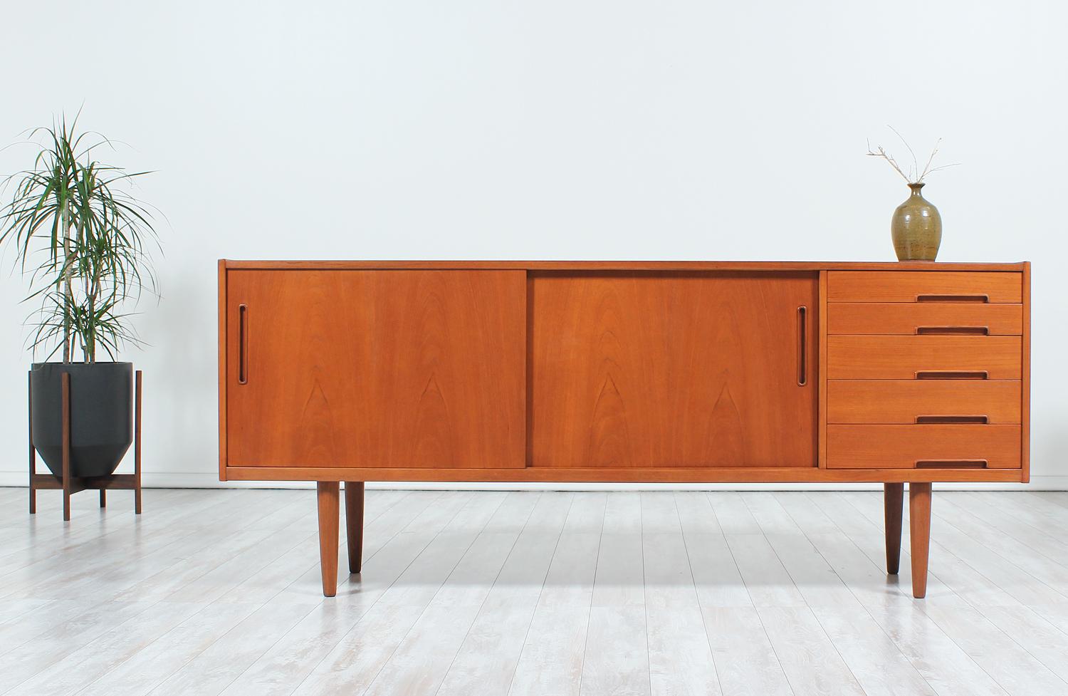 Gorgeous “Trento” credenza designed by Nils Jonsson for Hugo Troeds in Denmark circa 1960s. This clean design has been quality crafted in teak wood and features two sliding doors on the left side with two shelved compartments behind and five