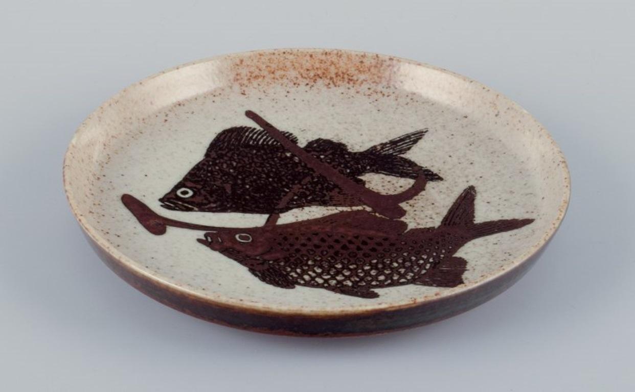 Nils Thorsson for Royal Copenhagen.
Unique ceramic dish decorated with fish. 
Glazed in brown tones.
Mid-20th century.
Signed.
Perfect condition.
First factory quality.
Dimensions: Diameter 19 cm x Height 2.5 cm.