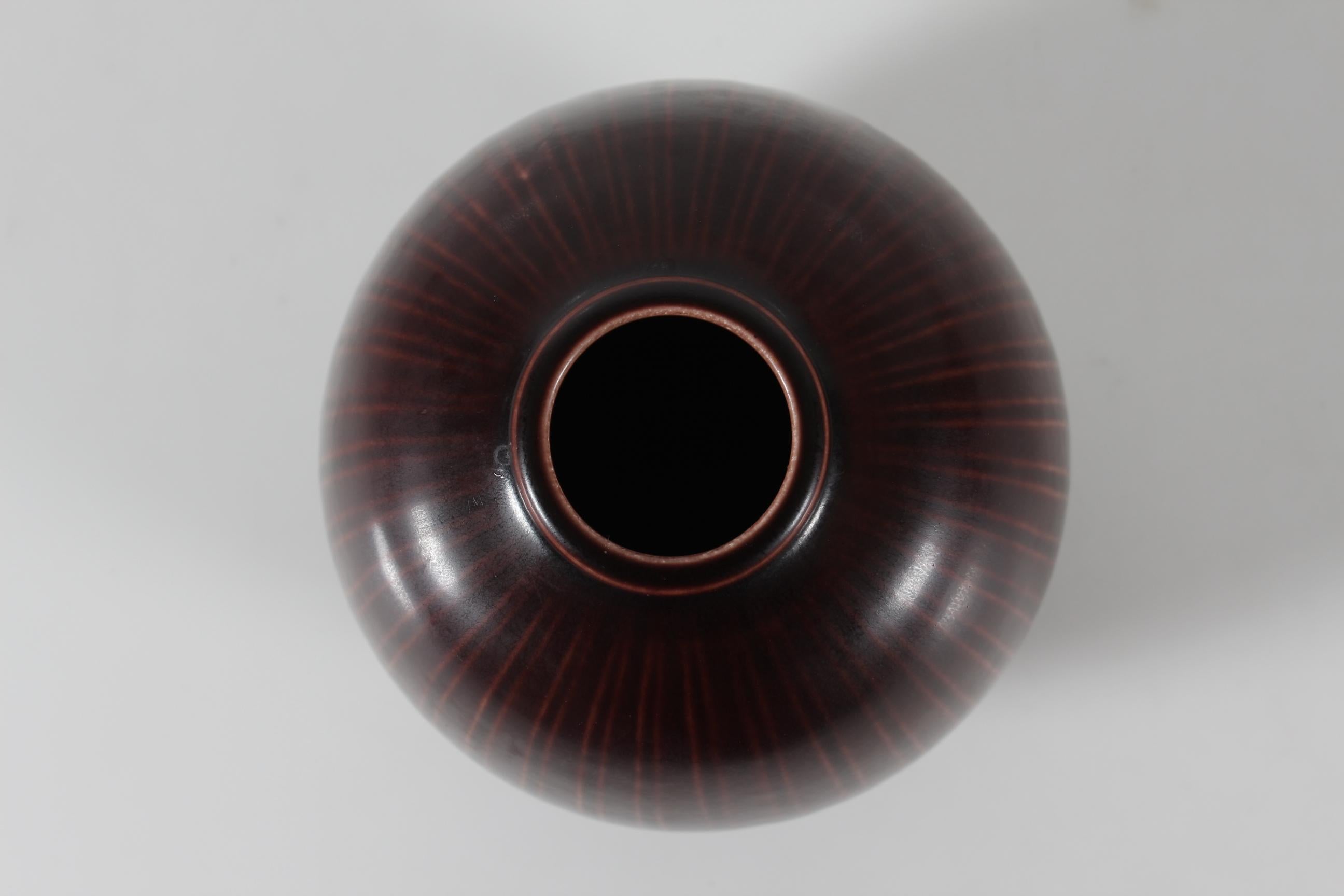 Marselis vase by Nils Thorsson (1898-1975) manufactured by Aluminia later Royal Copenhagen in Copenhagen, Denmark.

It's made of ceramic and features a maroon brown glaze over a stripe decor. The surface is tactile.

Nils Thorsson designed pieces