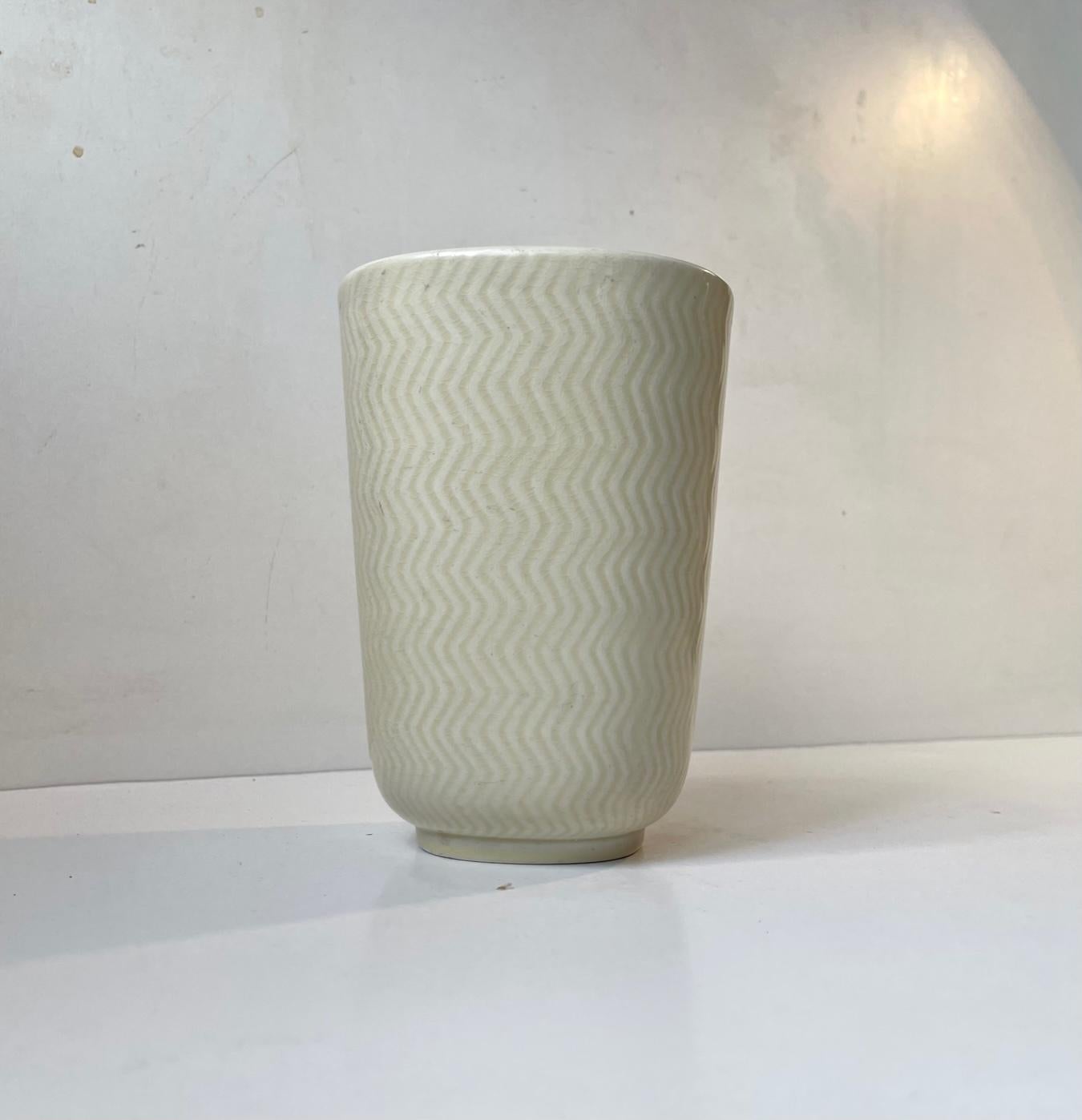 Ceramic/Faience vase designed by Nils Thorsson and manufactured by Aluminia in Denmark during the 1950s. It called Marselis 2645 and is decorated in pale yellow glaze upon a zigzag pattern. Measurements: H: 16 cm, D/W: 11.7 cm.