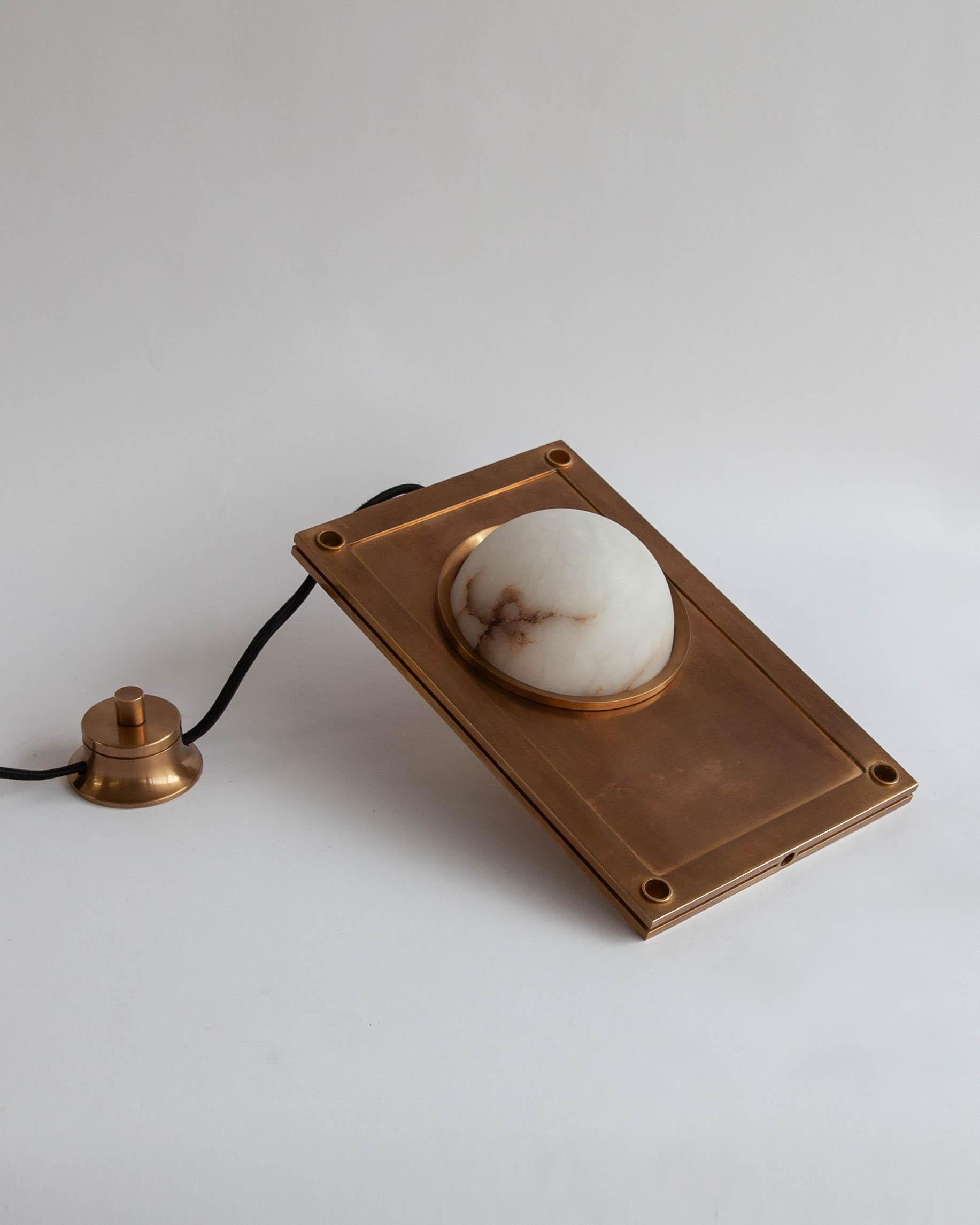 MTL4510 
An illuminated tabletop sculpture made of a hand-carved, veined white alabaster globe lens, set in a solid slab of machined brass with threaded porthole bezels. Fitted with a heavy brass rotary dimming switch and a single E12 LED lamp that