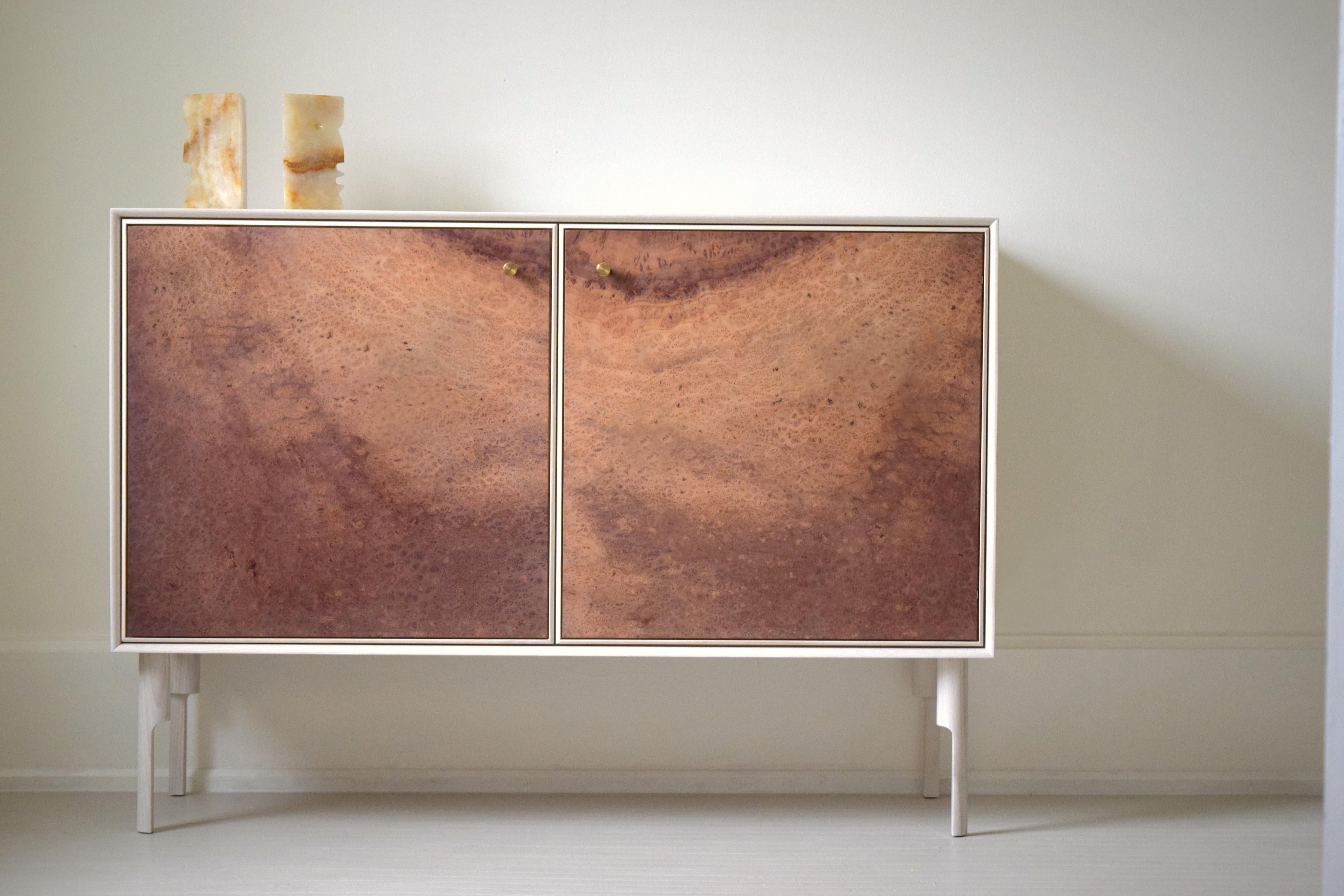 El armario Nina es una elegante vitrina de madera maciza disponible en varias frondosas norteamericanas, con puertas y frentes de cajón en pintura al aceite de linaza, laca o madera natural. La pieza presenta una caja ingleteada, patas torneadas a