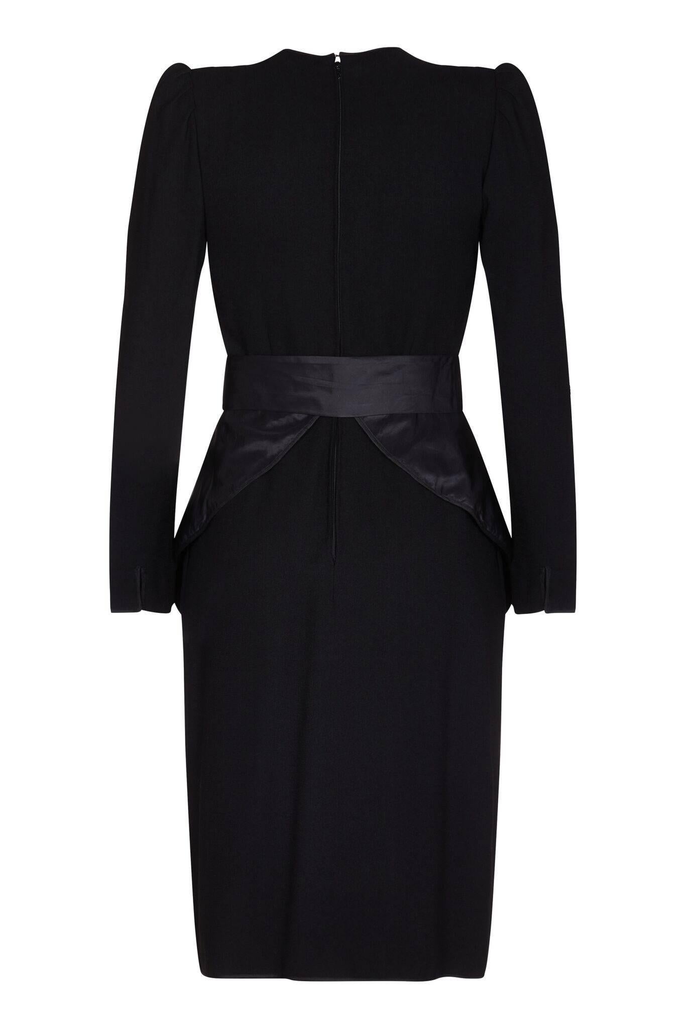 This dramatic Nina Ricci 1980s cocktail dress is a wonderful combination of feminine tailoring and statement design features. The dress is silk lined with a fine black wool crepe overlay and a silk taffetta peplum. The peplum is the key feature of