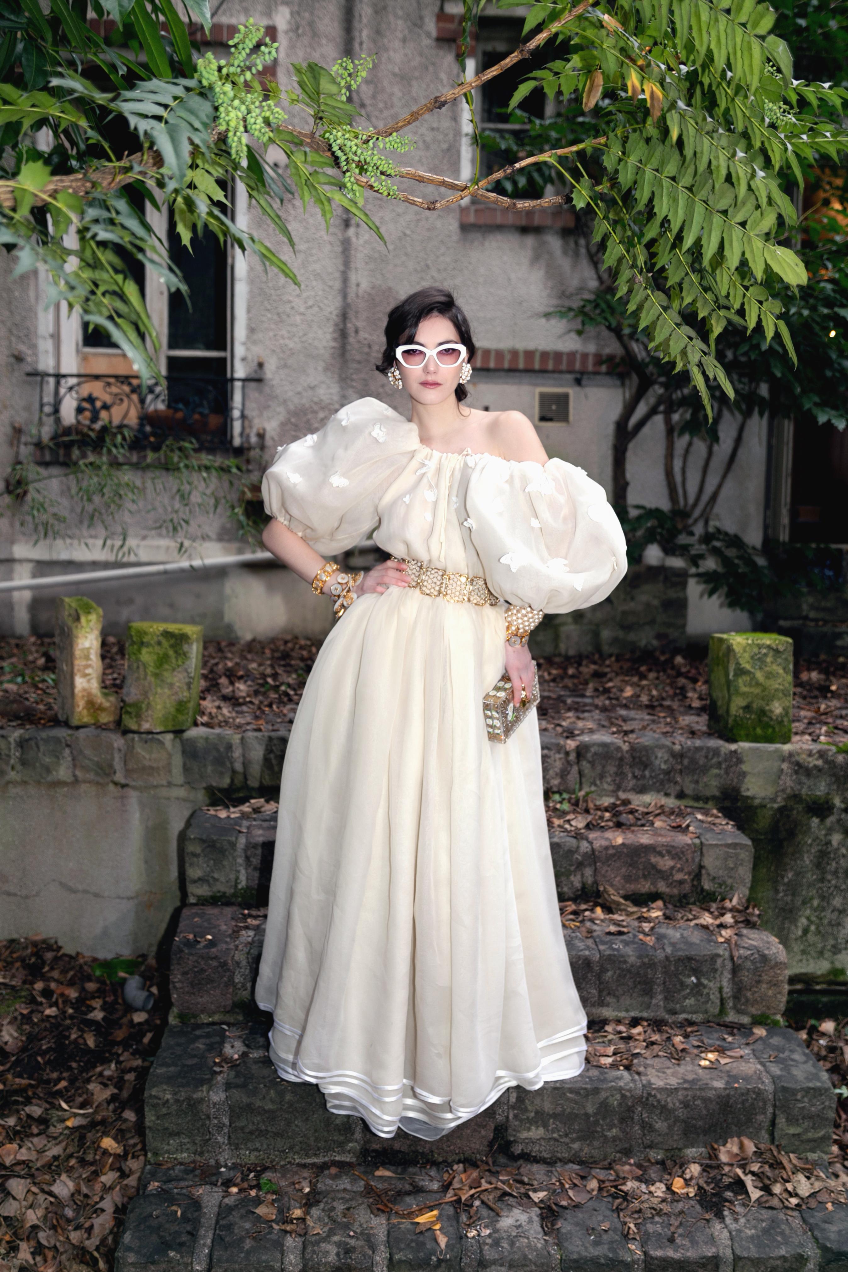 NINA RICCI - Beige organza dress with balloon sleeves decorated with white lace butterflies. The dress comes with a veil and a fuchsia-pink taffeta belt. No size indicated, it fits a 36FR. To be mentioned, there are few stains on the bottom of the