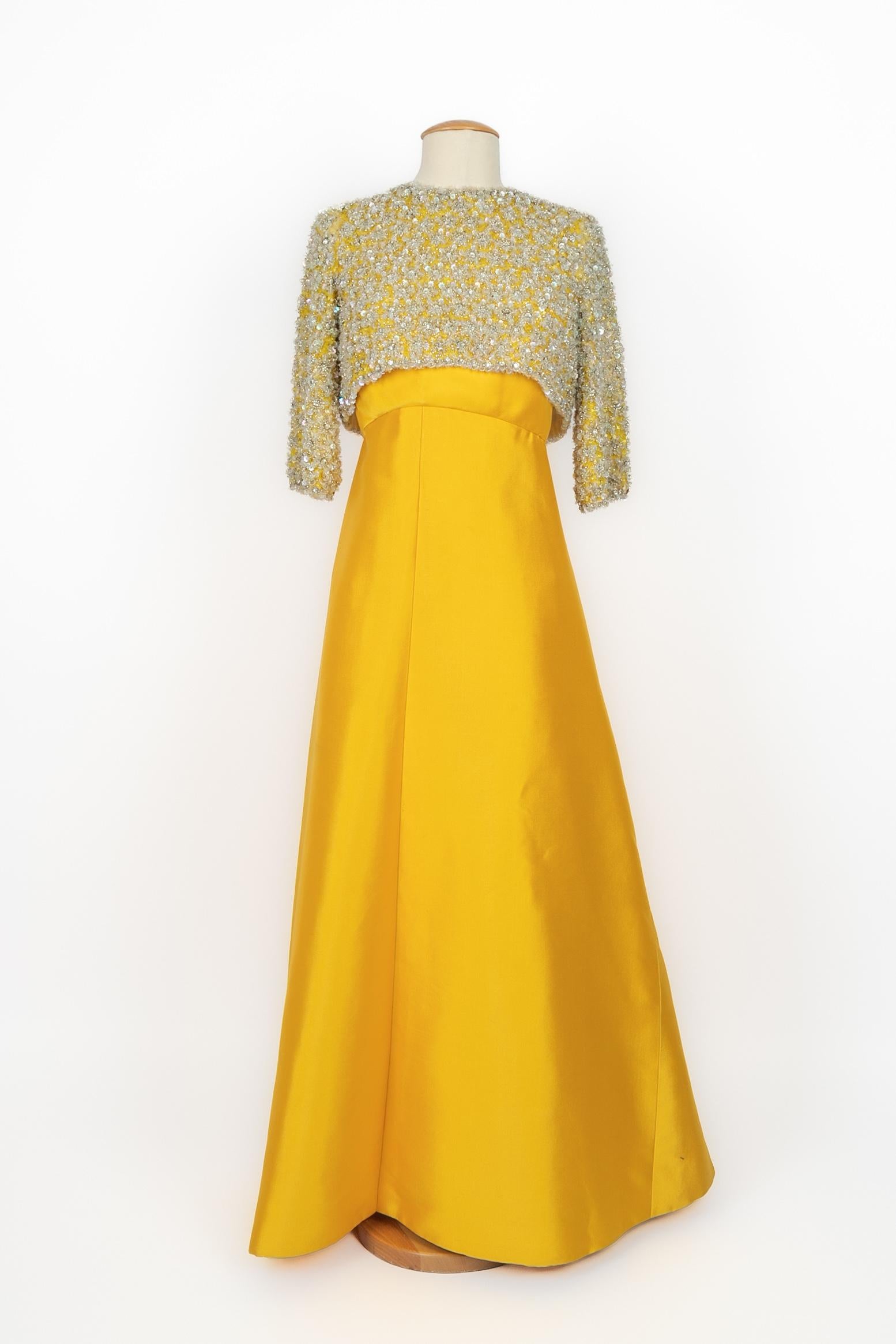 NINA RICCI - (Made in France) Gelbfarbenes Abendset aus Ziberline. Bustier-Kleideroberteil mit hoher Taille, über das eine locker sitzende, mit durchscheinenden Perlen bestickte Bluse gezogen ist. Bluse mit offenem Rücken, der die Schleife des