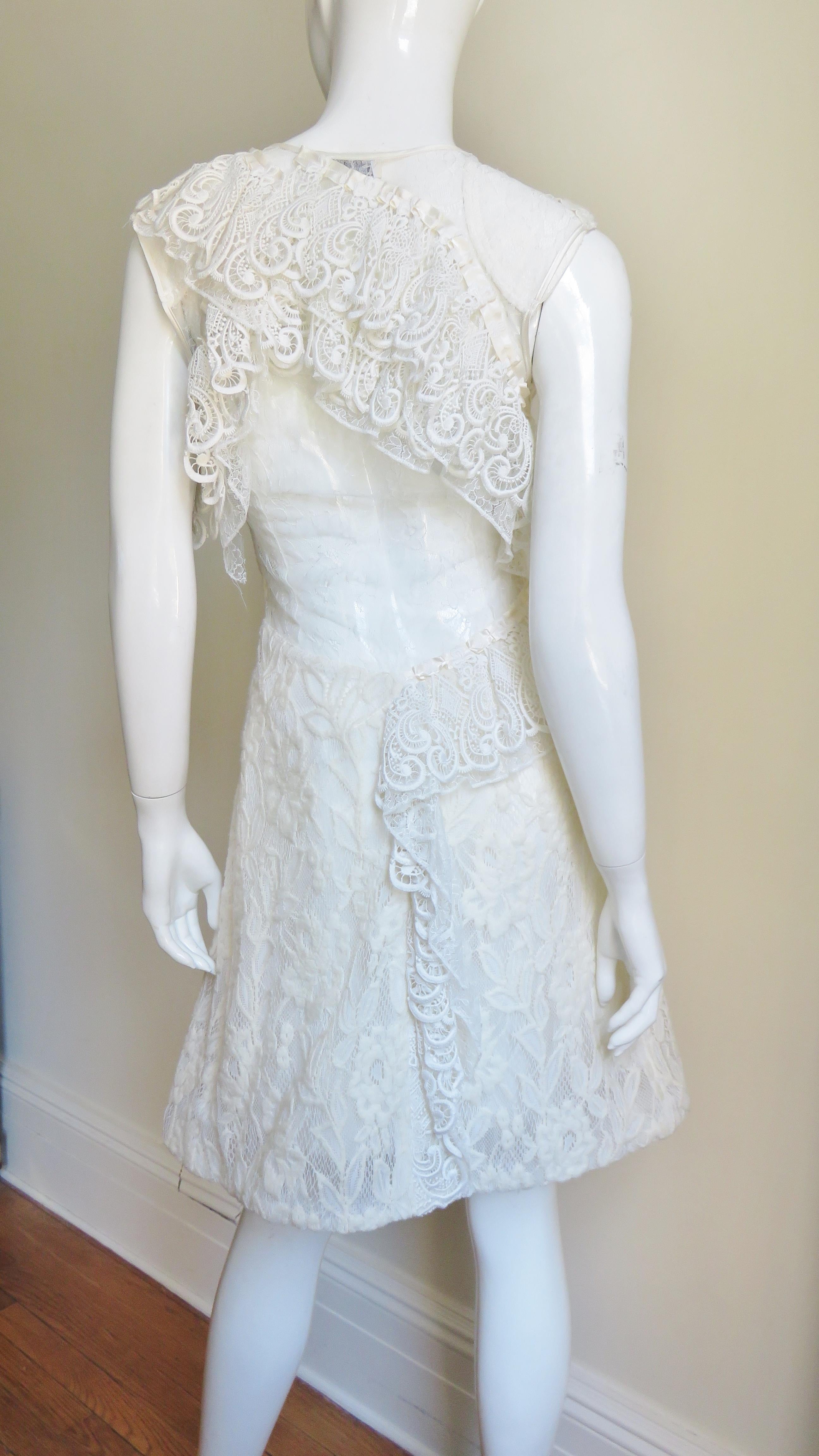 A gorgeous dress from Nina Ricci in elaborate white lace.  From the front it is a simple V neck sleeveless A line dress.  The back has a lace covered cut out from below the waist to the shoulders framed with lace ruffles. It has a side zipper.
Fits