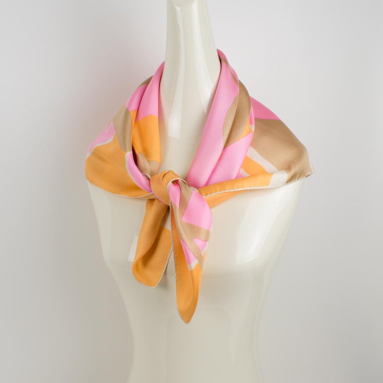 Elegant silk scarf by Nina Ricci Paris in pink and orange colors featuring floral abstract 1970s design print. Nina Ricci Paris's signature name on the lower right corner. The colors are bright and vibrant with a combination of ballet sleeper pink,