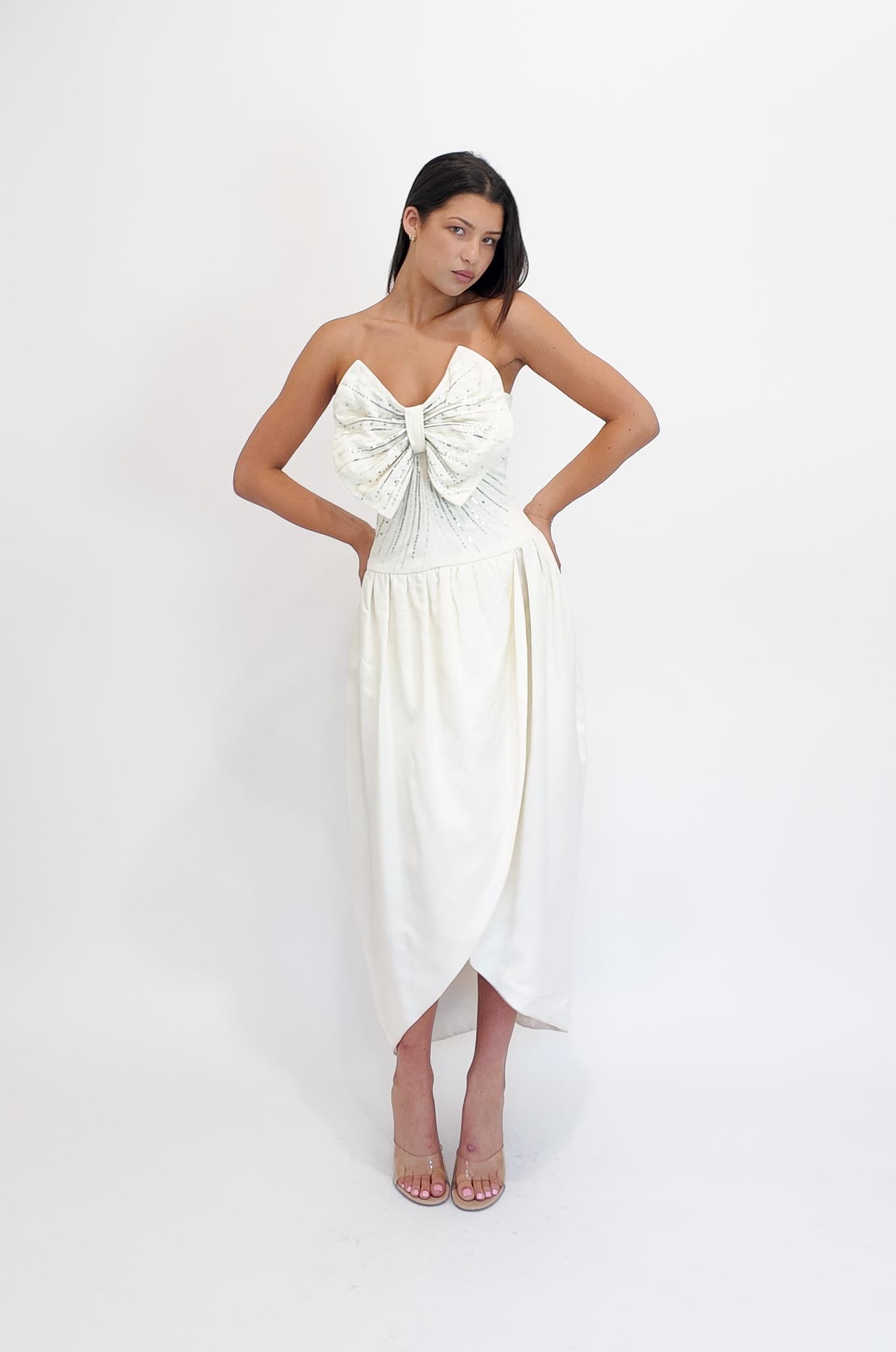 Cette robe en soie blanche de Nina Ricci est dotée d'un corsage à gros nœuds qui ajoute un charme raffiné et pudique à sa silhouette traditionnelle. Confectionné en soie luxueuse, il incarne l'élégance intemporelle, ce qui en fait un choix exquis