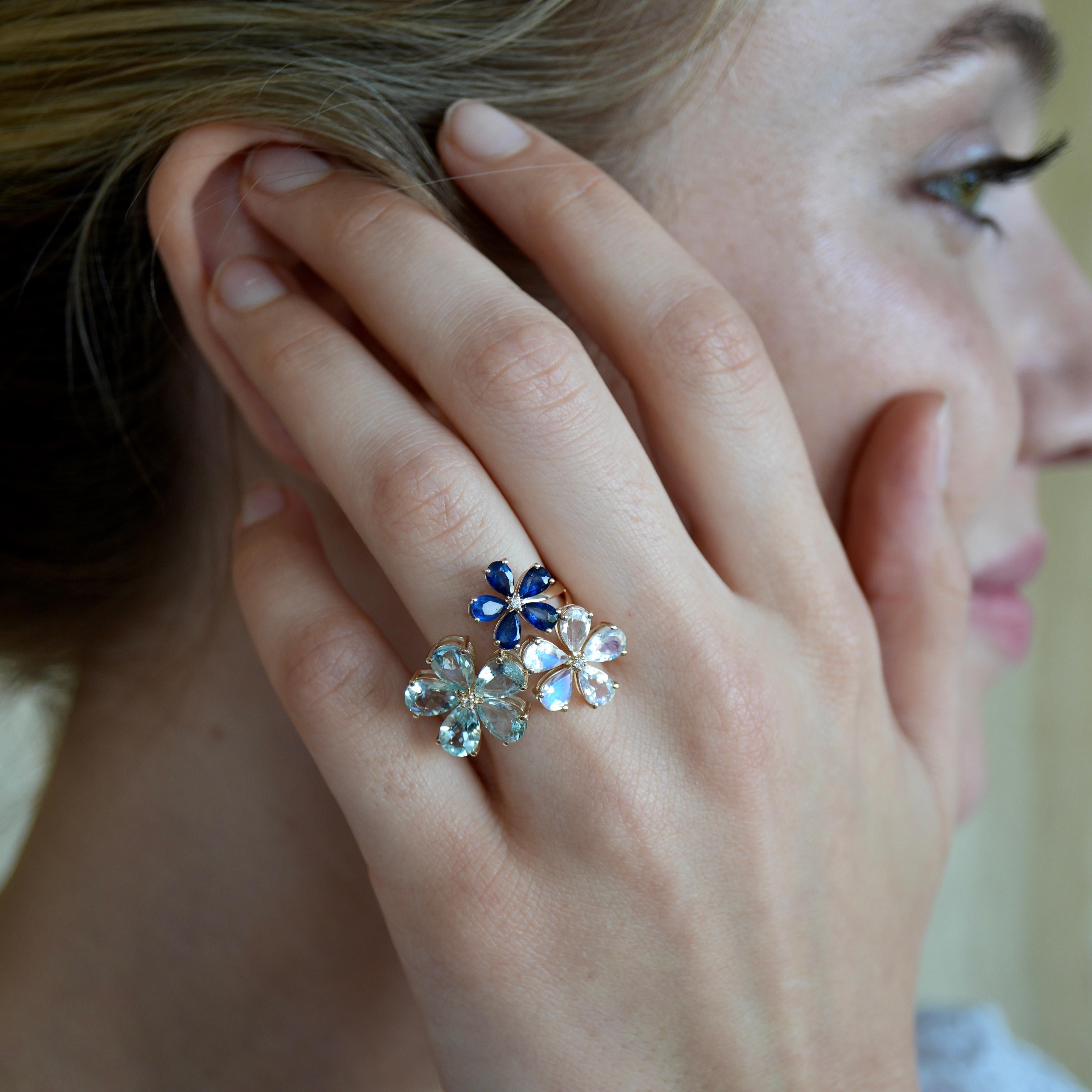 Scopri l'anello Nina Zhou Aquamarine Moonstone Sapphire Diamond Flower Blossom, un'incantevole opera d'arte che mette in mostra la brillantezza dell'acquamarina, la bellezza mistica della pietra di luna e il fascino profondo degli zaffiri.