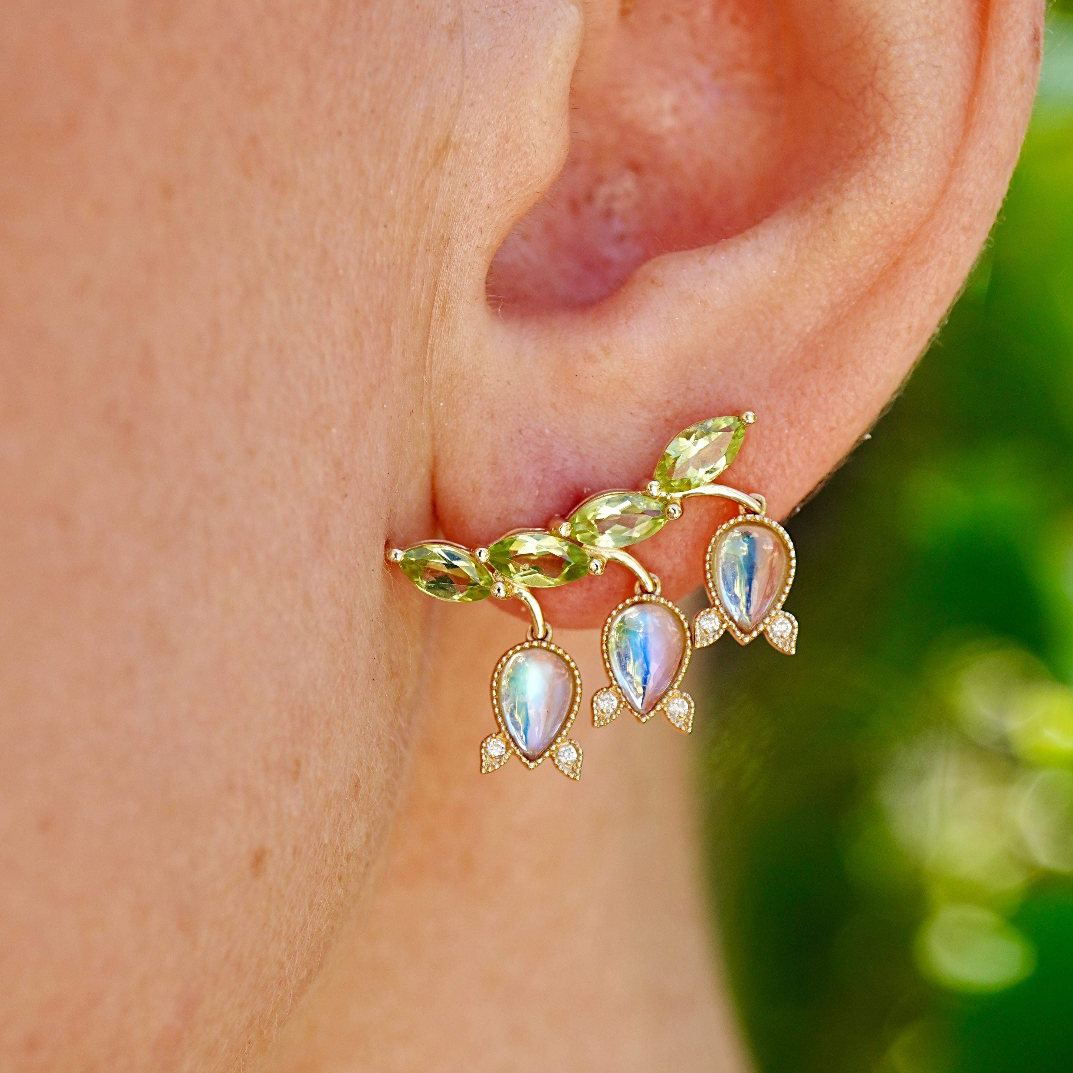 Ispirati al grazioso arco degli steli di mughetto, questi orecchini fondono la forma botanica con l'artigianato. Sei pietre di luna arcobaleno tagliate a pera brillano di iridescenza blu, mentre otto peridoti tagliati a marquise evocano la