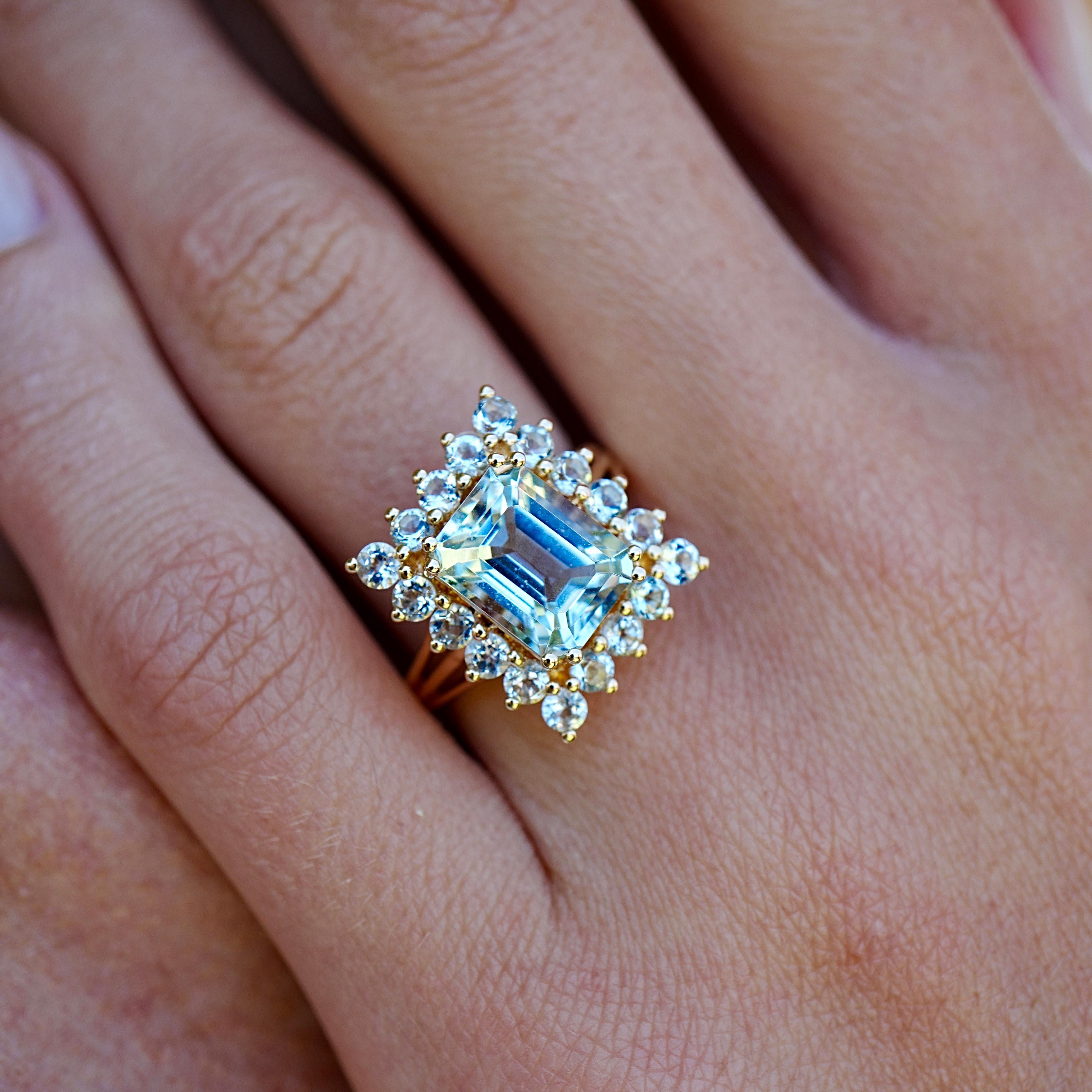 Dieser Nina Zhou Margaret Aquamarin-Cocktailring ist ein echtes Statement, das die Schönheit von Licht und Bewegung einfängt. In seinem Zentrum leuchtet ein lebendiger Aquamarin in einem kühlen, ruhigen Blau, umrahmt von einem Halo aus weiteren