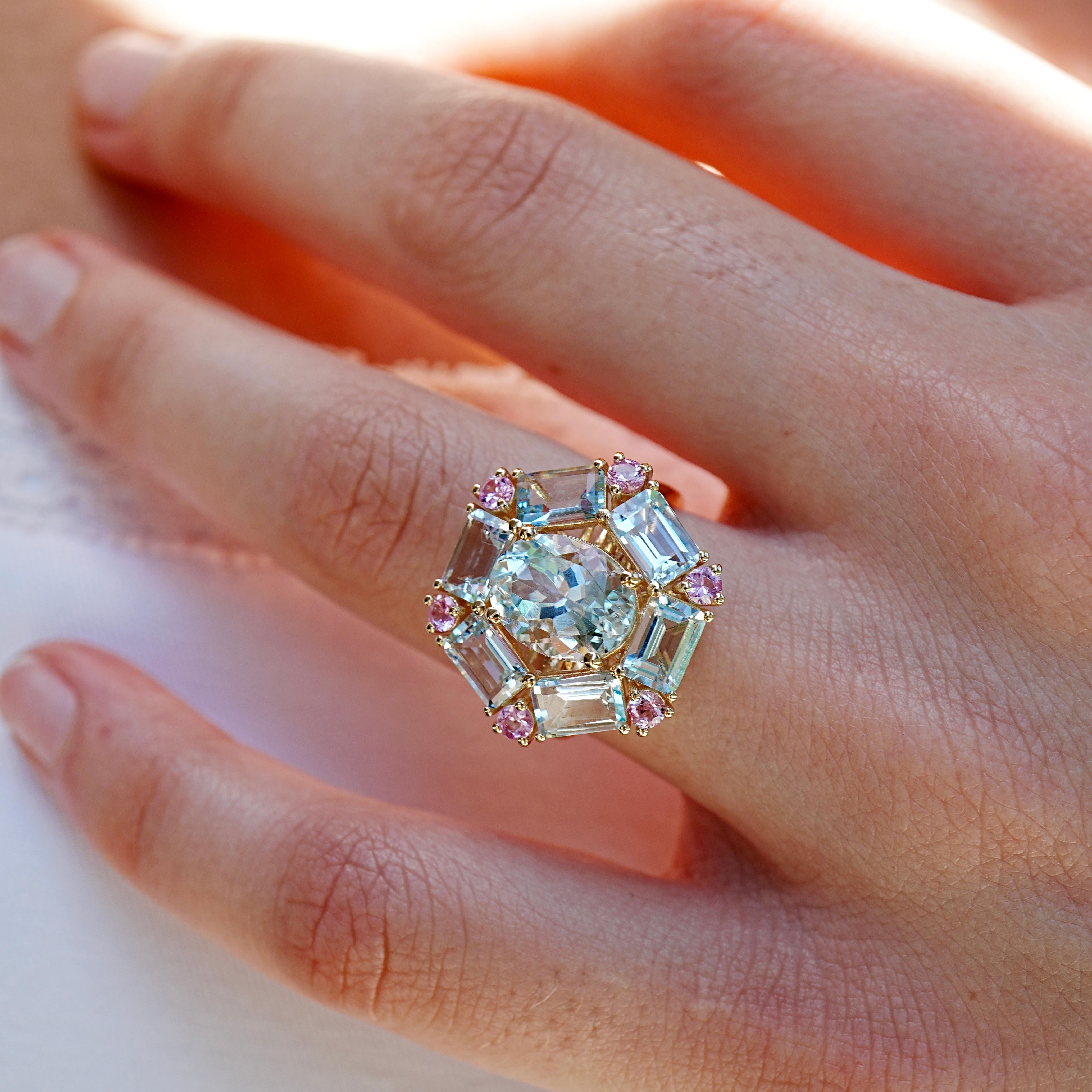 Der Cocktailring Margaret mit 5,60 ct Aquamarin und rosa Saphir strahlt Eleganz und Charme aus und ist ein Fest der Farben und der Kunstfertigkeit. In der Mitte schimmert ein atemberaubender ovaler Aquamarin mit der ruhigen Schönheit eines klaren