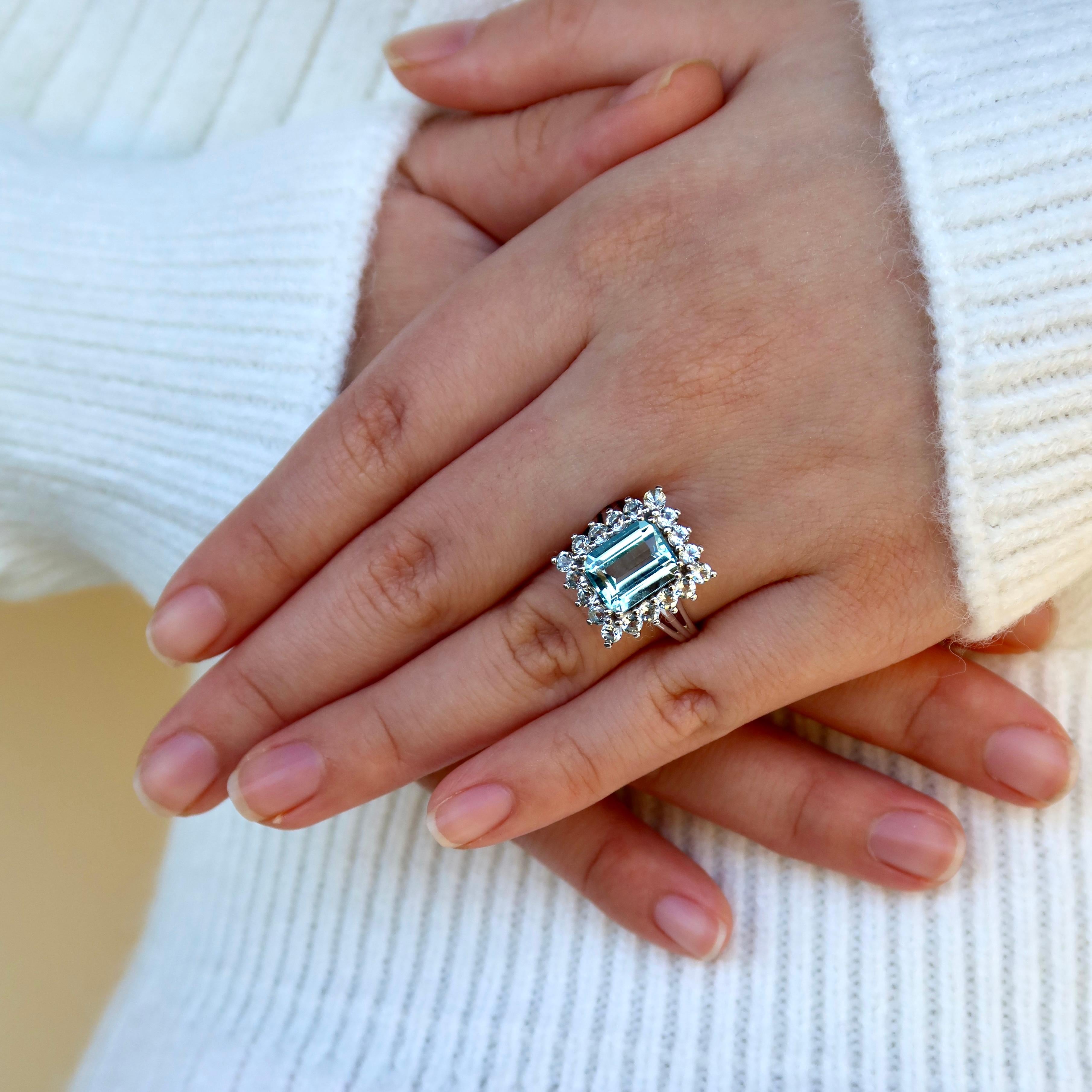 This Nina Zhou Margaret 4.50 ctw Aquamarine Cocktail Ring is a true statement piece, designed to capture the beauty of light and movement. At its center, a vivid aquamarine glows with a cool, tranquil blue, framed by a halo of more aquamarine that
