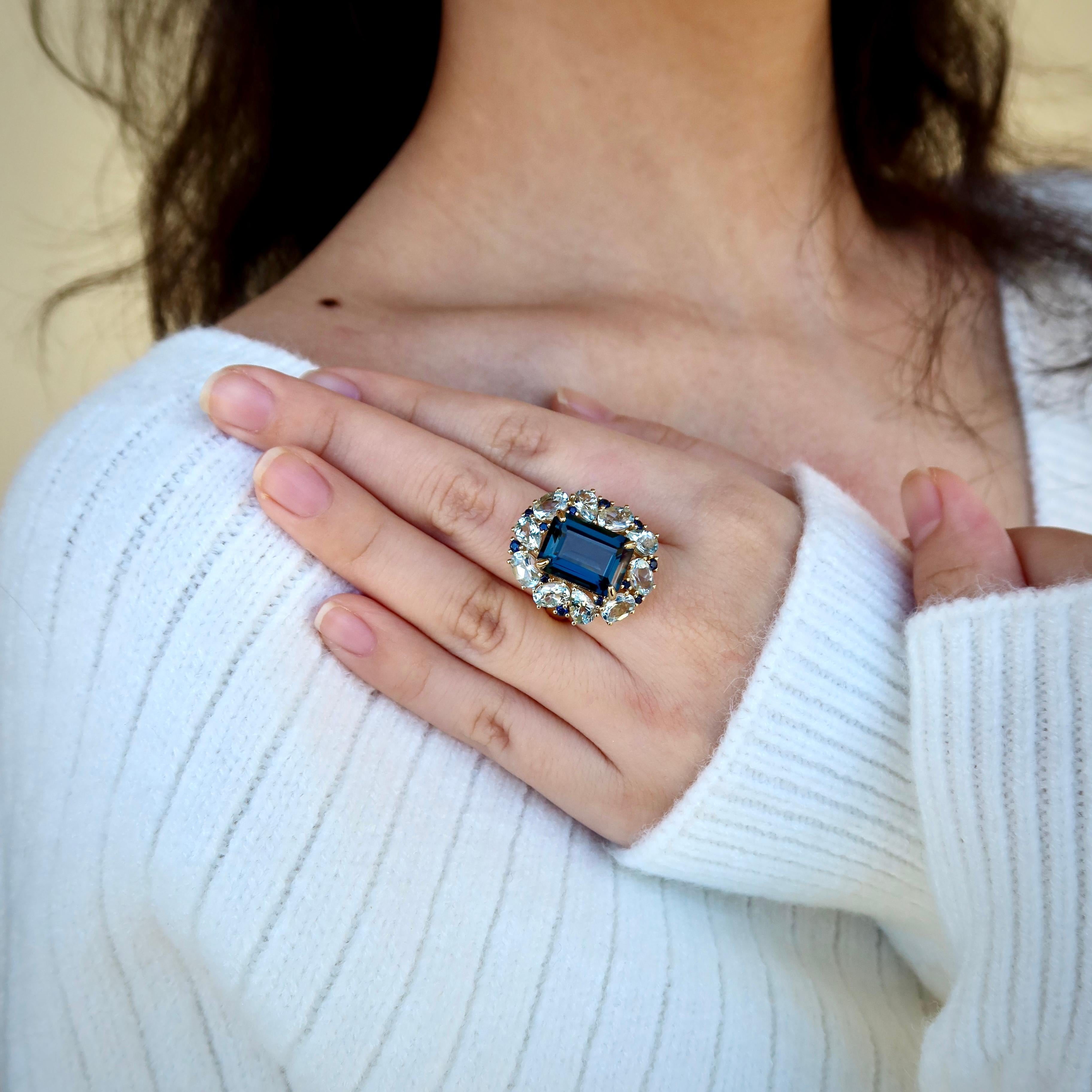 Ti presentiamo l'anello da cocktail Margaret London Blue Topaz Aquamarine Sapphire, un capolavoro di eleganza e opulenza. Realizzato in lussuoso oro massiccio, questo anello ha al centro uno splendido Topazio Blu di Londra dal taglio a smeraldo, che