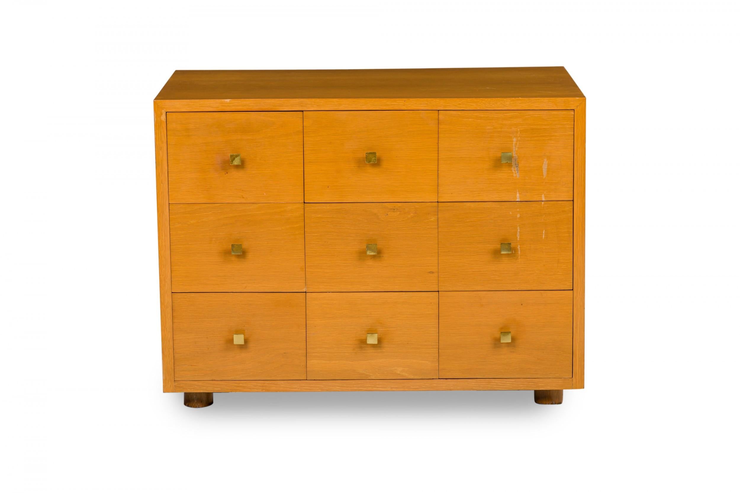 American Mid-Century maple bedside table / commode with nine small drawers with square brass drawer pulls resting on four small square feet.