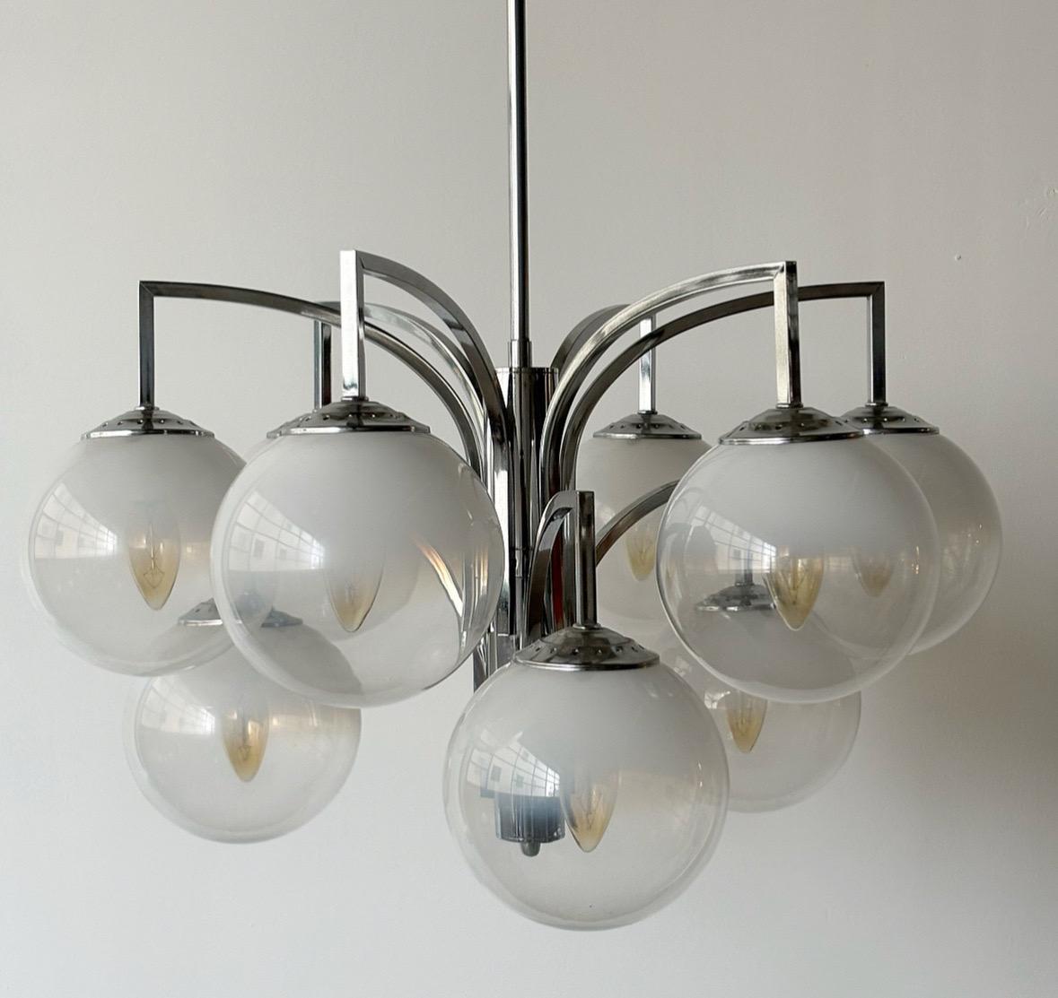 Ce lustre, conçu dans les années 1970 et fabriqué par Design/One, est un exemple étonnant de l'artisanat moderne du milieu du siècle. Sa structure, en acier chromé de haute qualité, met en valeur neuf bras élégamment courbés, chacun se terminant par