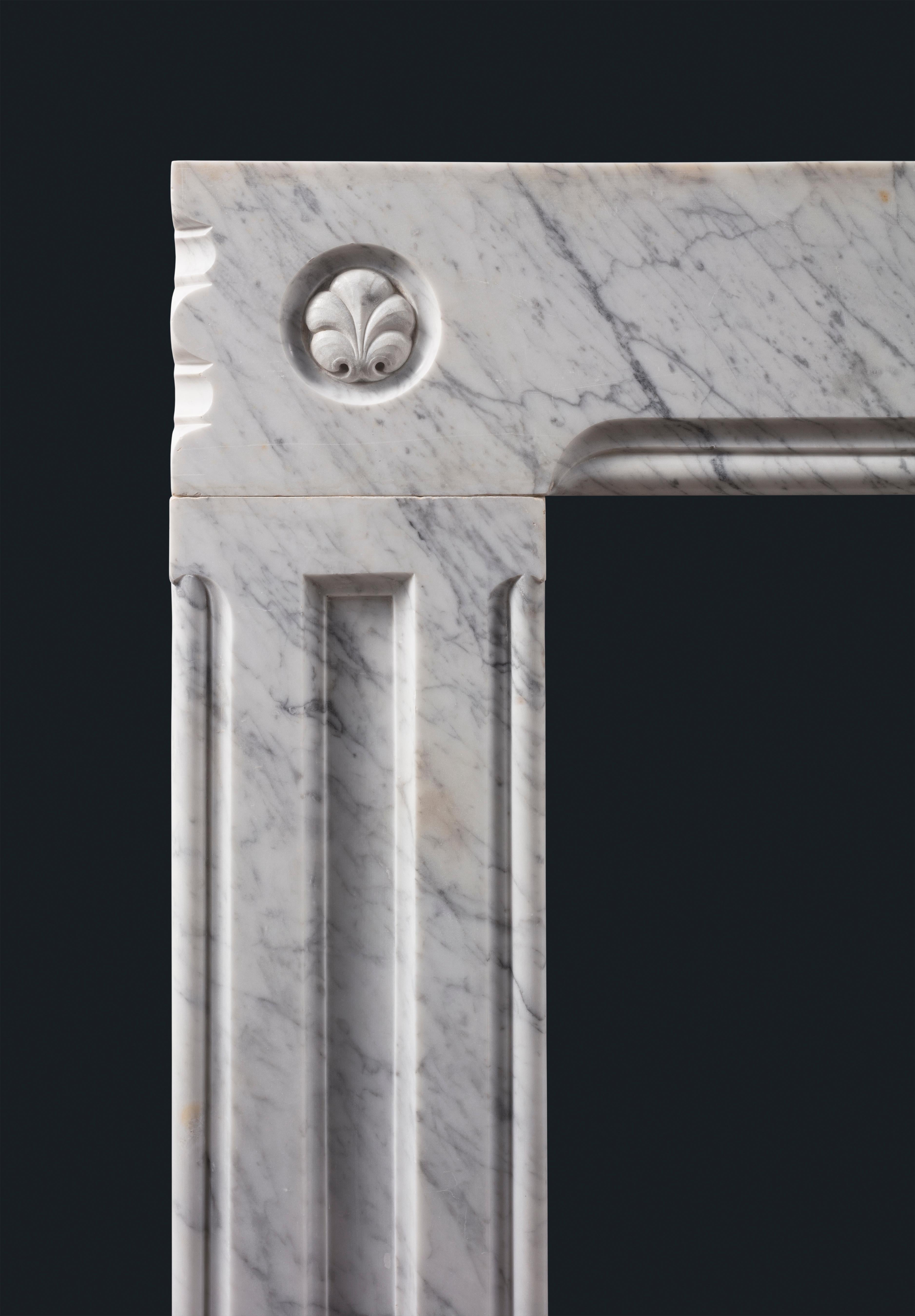 A well carved antique Carrara marble frame fireplace surround with stylised fleur-de-lys set in circular frames to each corner, the fielded panel jambs and frieze each outlined with generous double mould. 

Early nineteenth century, by repute from