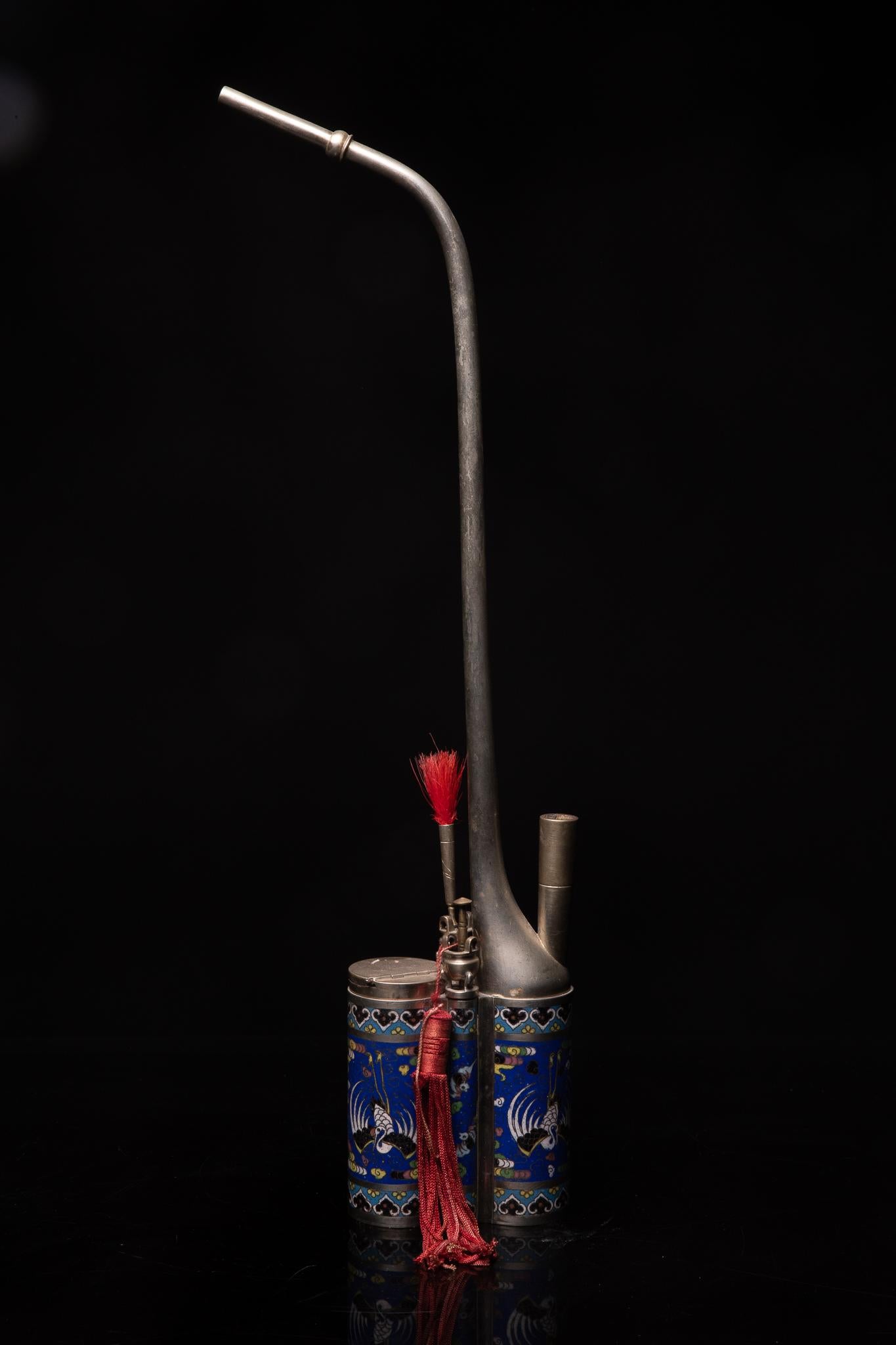Nineteenth century Chinese water pipe in Paktong (= an Alloy of Zinc, Copper and Nickel). The Base - elaborated in Enamel Cloisonné - is decorated with a Phoenix on an Ultramarine Blue Background. The Accessory Holders have the Form of Incence