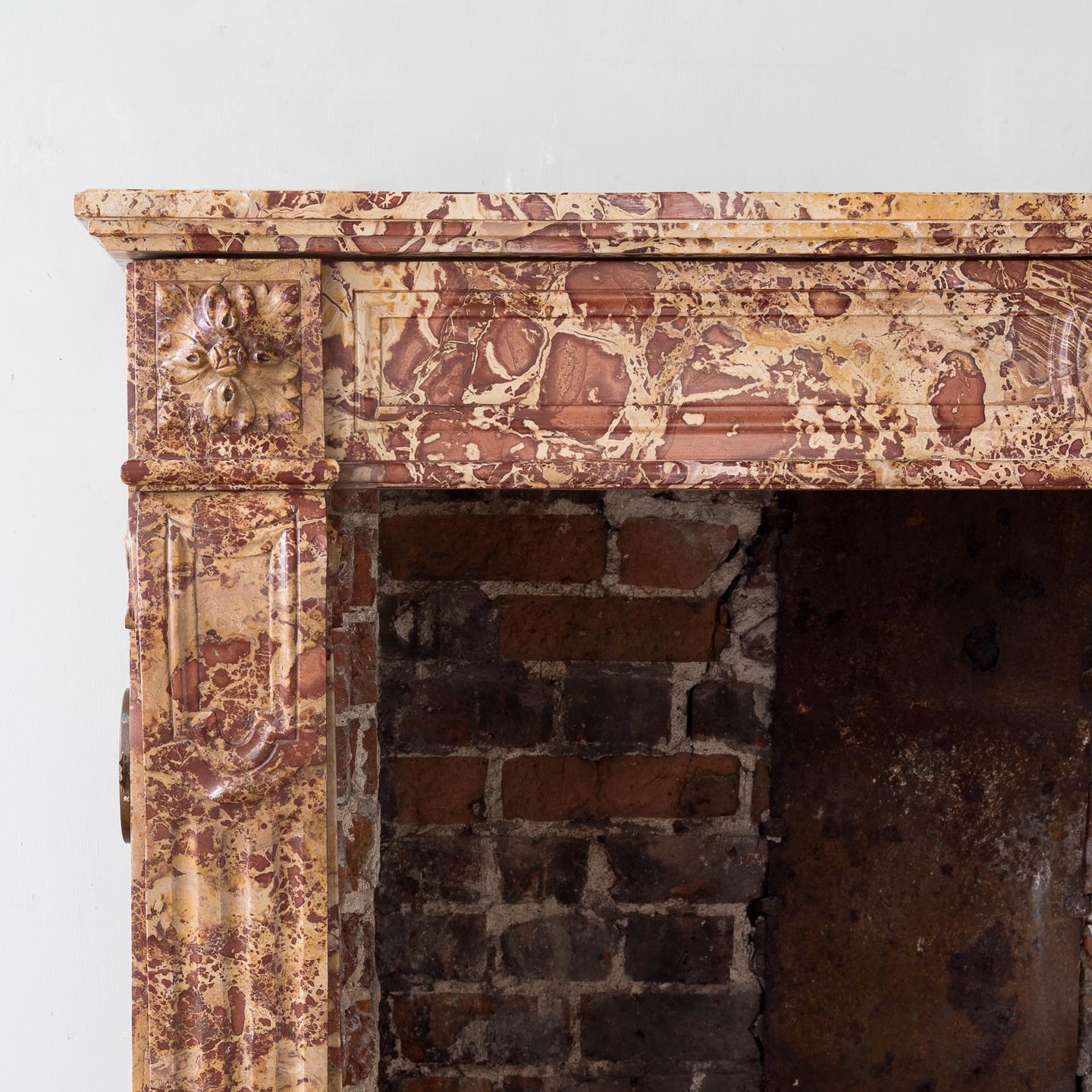 19th century French Breche fire surround, in the Louis XVI style, the paneled frieze centred by foliate boss, the paterae corner-blocks above stop-fluted console jambs, on block feet.

Measures: Aperture width 112cm x 88.5cm high.