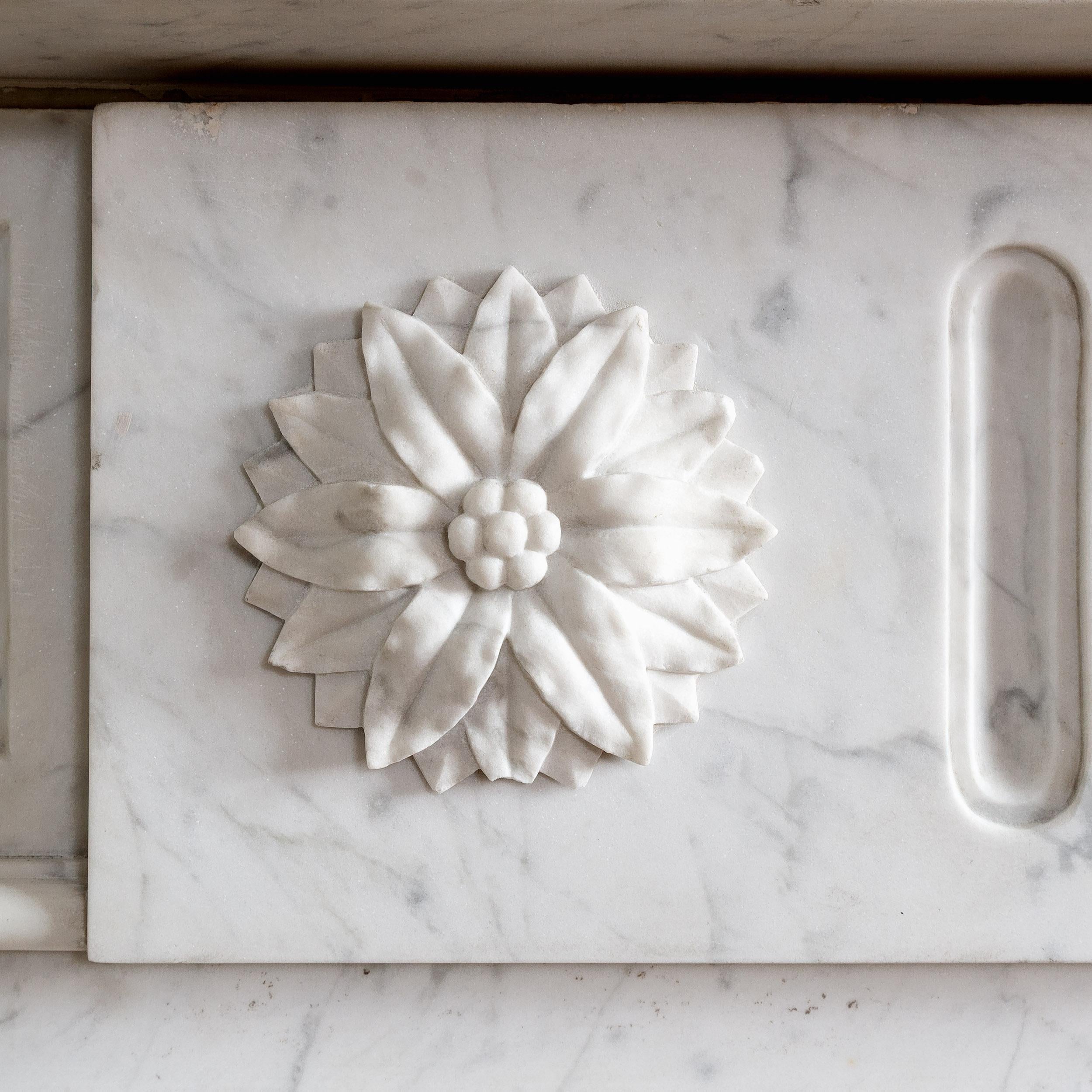 A large nineteenth century French Carrara marble fireplace, the moulded, breakfront shelf above frieze with a central tablet carved with flutes and foliate paterae, the stop-fluted quarter-round jambs raised on footblocks, with inverse ogee frame