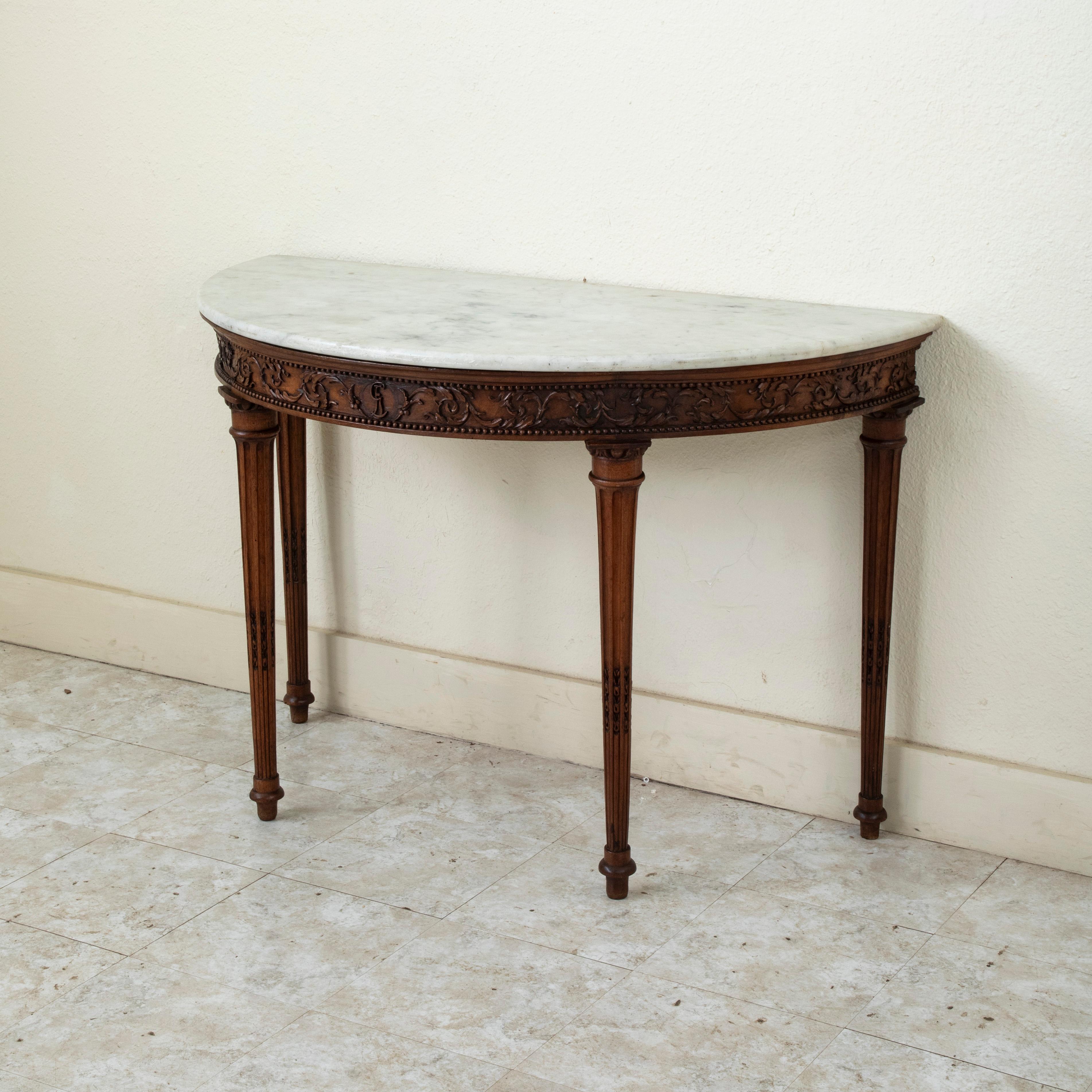 Proveniente dalla città di Arles, nel sud della Francia, questa consolle demi-lune in noce della metà del XIX secolo presenta un piano in marmo bianco. I dettagli intagliati a mano sul grembiule sotto il piano includono un monogramma centrale con le