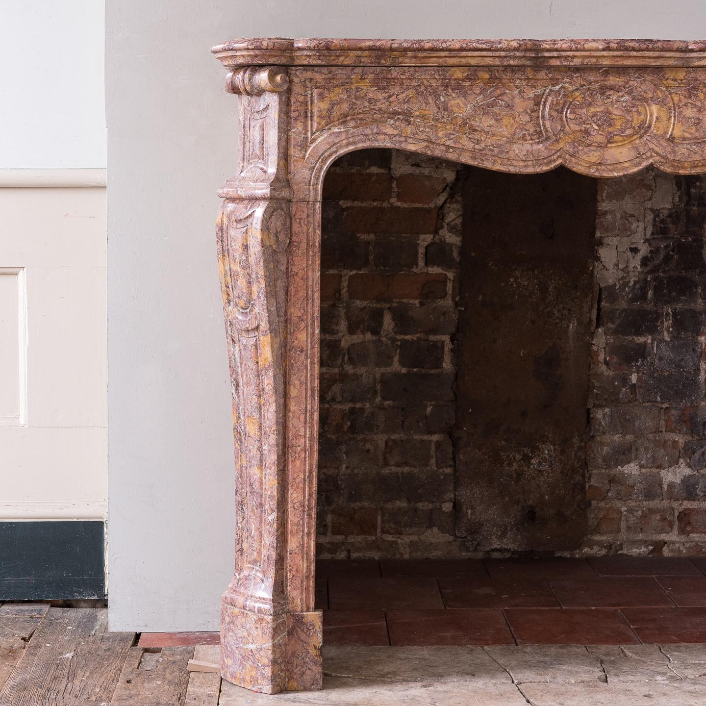 A nineteenth century French Pompadour fireplace, carved in Spanish Brocatello marble, the moulded and shaped shelf above panelled frieze on canted volute jambs. Wonderfully rich material.

Opening width 96cm x 91cm high, outside jamb to jamb width