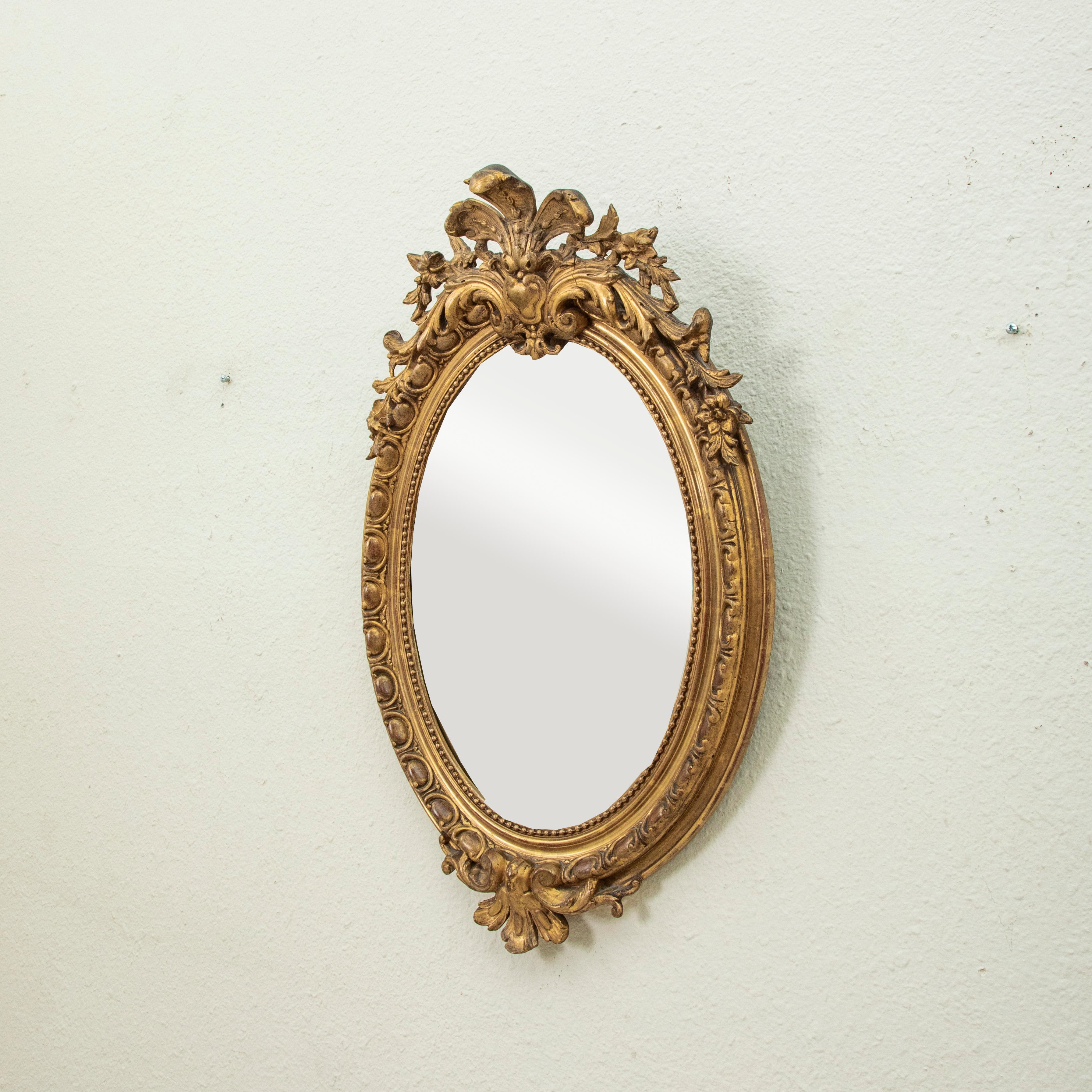 This nineteenth century French Regency style oval gilt wood mirror features beveled glass and a symmetrical palmette at the crown flanked by acanthus leaves and flowers. The frame is detailed with an egg and dart pattern with an inner border of