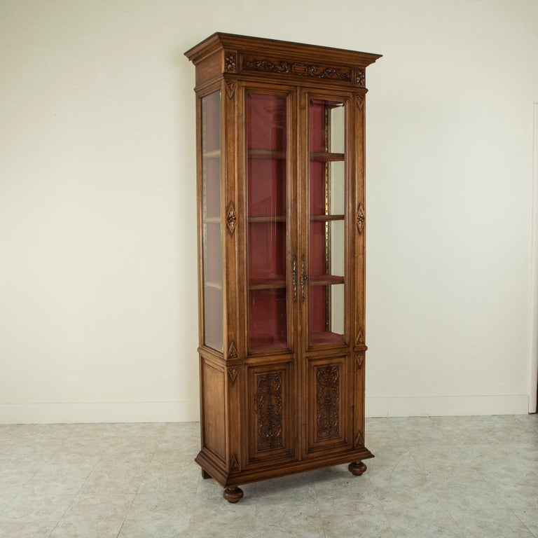 Standing at just over seven feet in height, this tall, narrow French Henri II walnut vitrine features beveled glass on three sides. Hand carved rosettes detail the sides and corners, and the doors are decorated with lower panels of hand carved