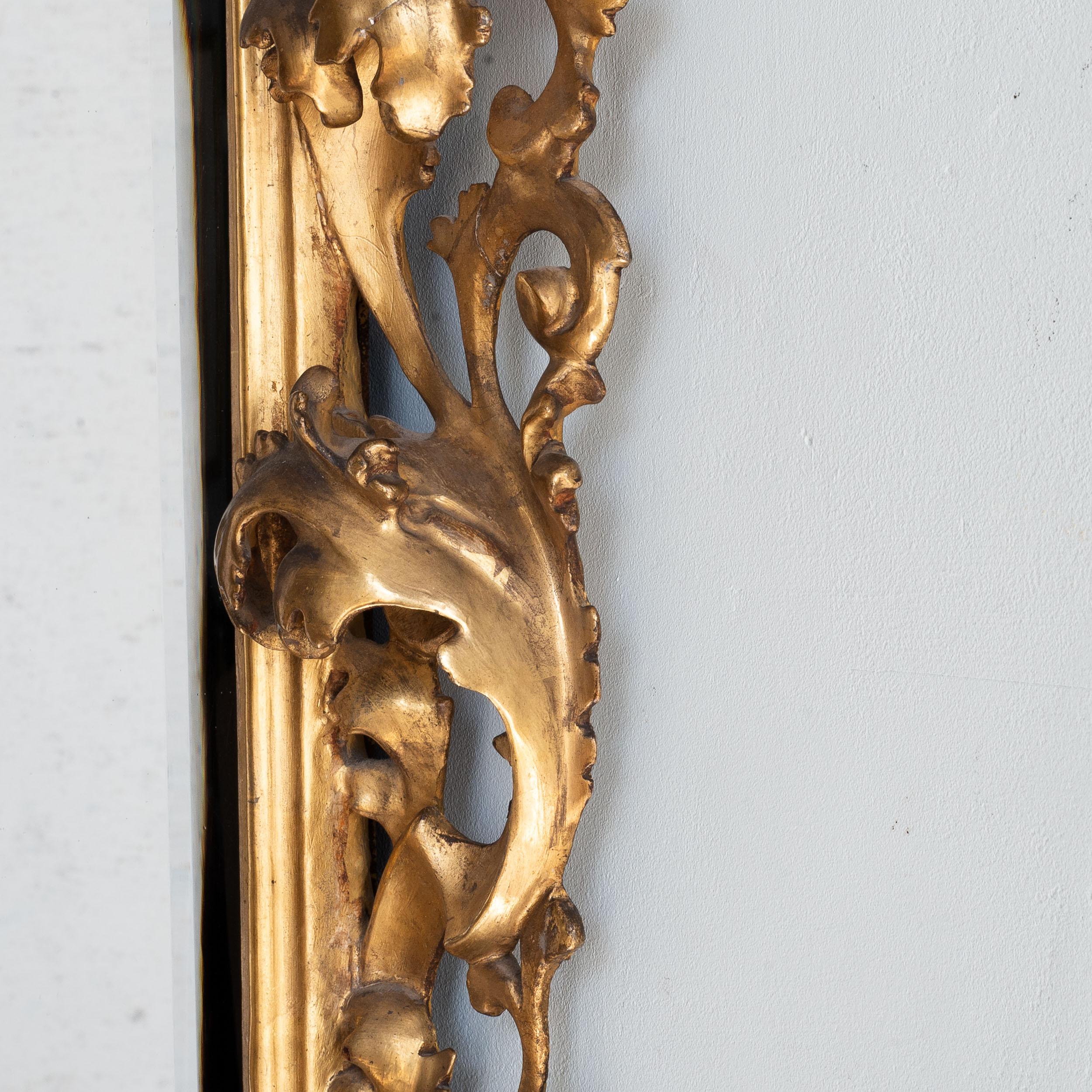 Un Florentine italien du dix-neuvième siècle  miroir en bois doré, le cadre audacieusement sculpté, gesso et doré avec plaque de miroir d'époque, avec une large crête de feuilles au sommet, menant à des volutes A.I.C. élaborées de chaque côté, et