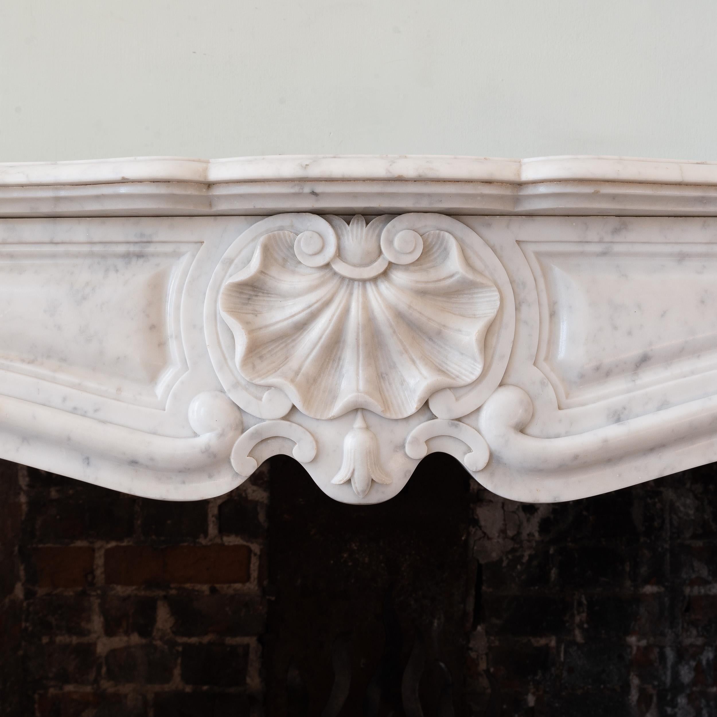 Chimenea rococó francesa de finales del siglo XIX, de estilo Luis XV y tallada en mármol italiano de Carrara, con una concha de vieira en el centro del friso perfilado, las jambas en forma de voluta giradas hacia fuera con otros cierres de concha de