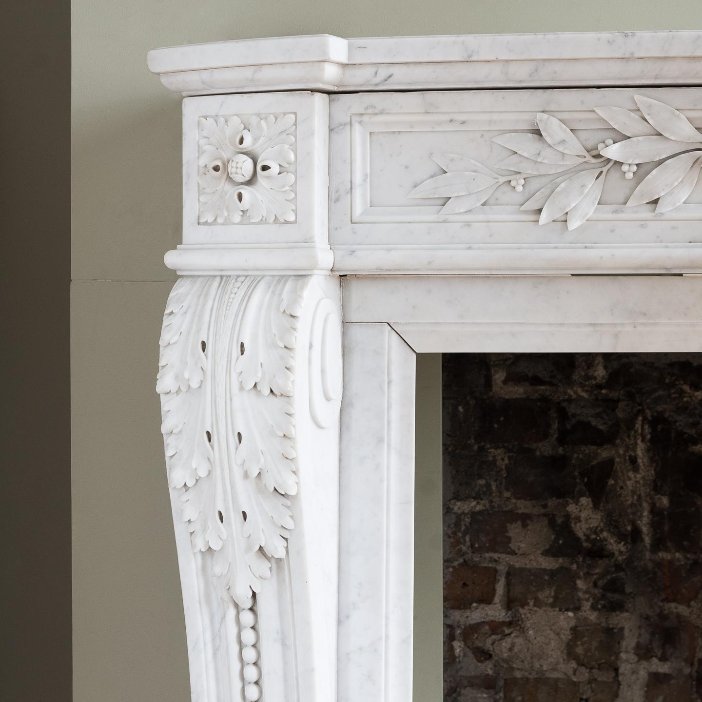 A fine Louis XVI style Carrara marble chimneypiece, the bowed breakfront shelf above finely carved frieze of laurel leaves and bowed ribbon, the square paterae end blocks above outswept acanthine volute jambs with channel moulded and beaded