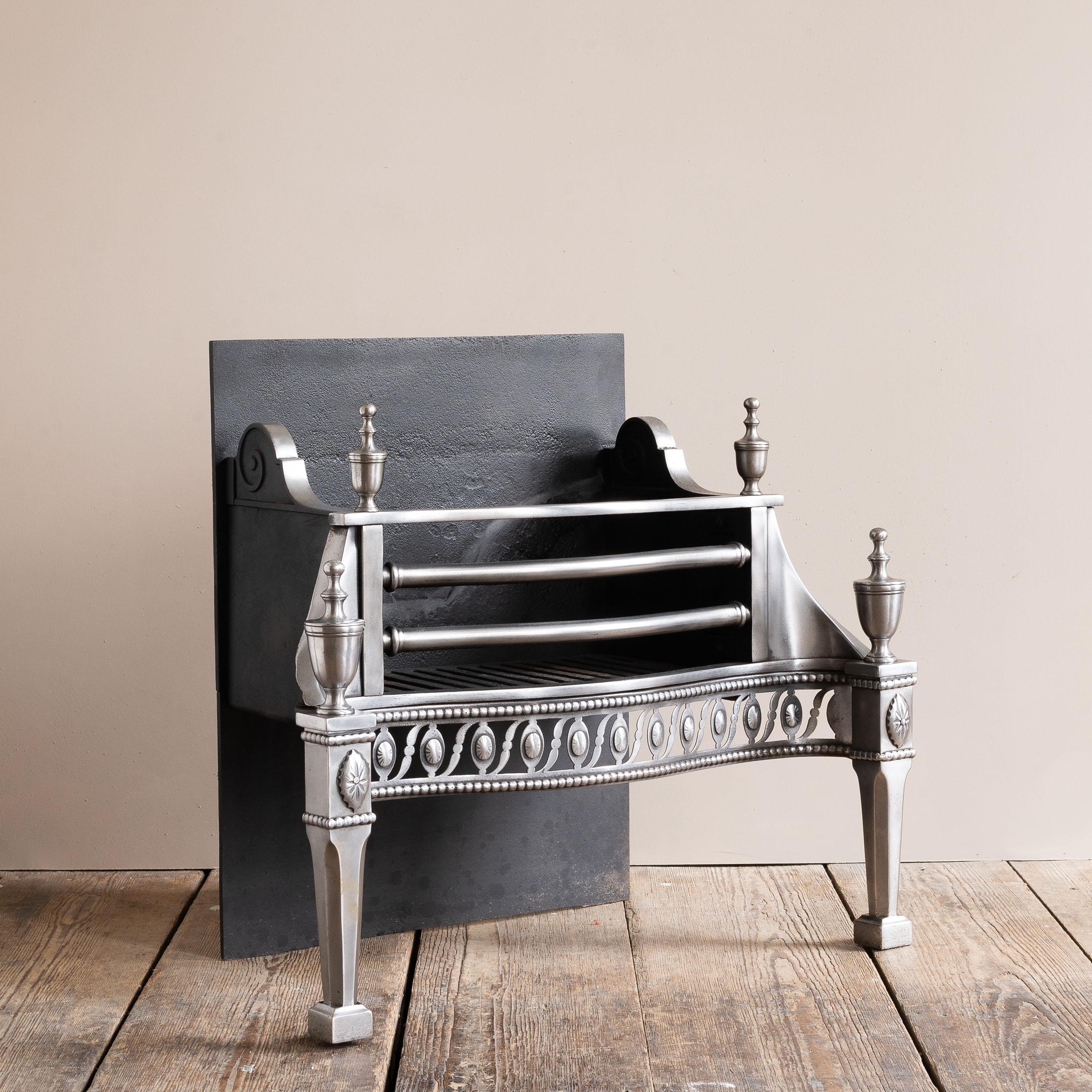 A nineteenth century polished steel and iron fire grate, in the George III style with urn finials and oval paterae to the serpentine fret.

Dimensions:	63.5cm (25