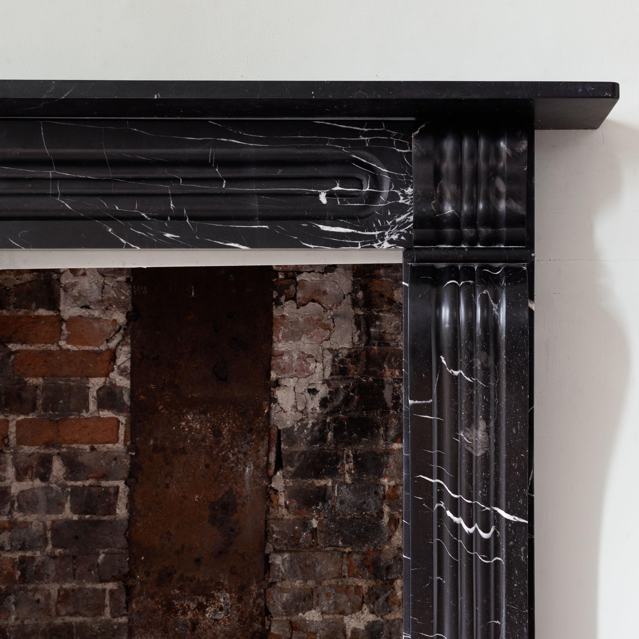 Cheminée en marbre et calcaire Radford Black d'époque George IV, vers 1820-30,
la frise lambrissée avec des corbeaux façonnés à chaque angle, les montants de la console audacieusement chantournés et moulurés sur des pieds en bloc. Remplacement de