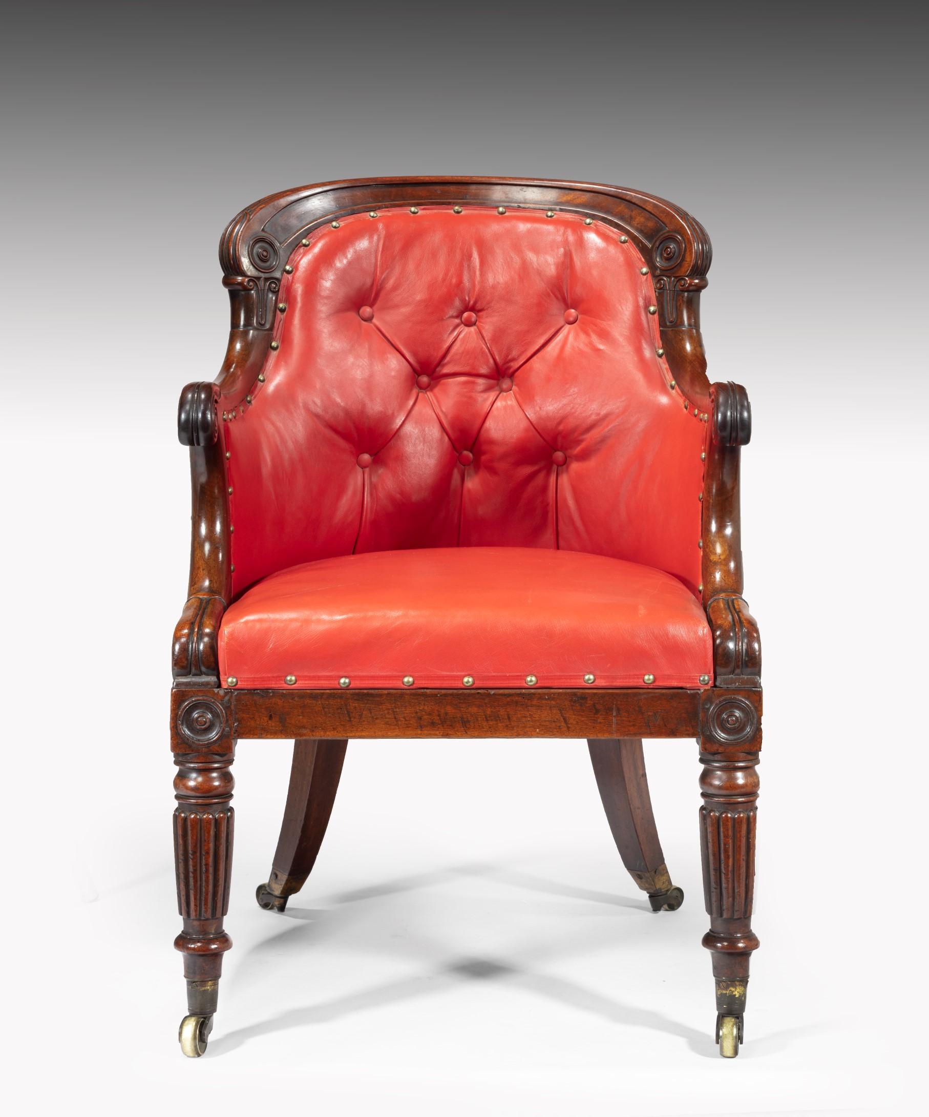 A superb Regency period mahogany desk armchair upholstered in red leather, the armchair's mahogany show-wood frame carved crisply carved with lotus leaves to the arms and raised on turned and reeded legs which terminate in the original brass cap