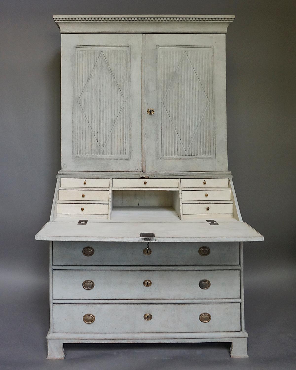 Period neoclassical secretary in two parts, Sweden circa 1840. The upper section has a straight cornice with dentil molding and double doors with raised, reeded panels with incised lozenges. Inside are three shelves with a central divider. The lower