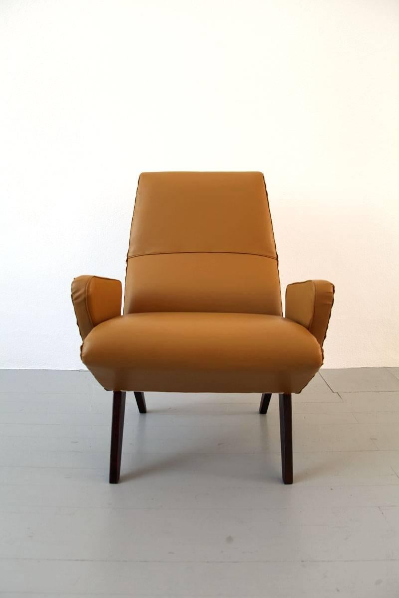 This armchair was designed by Nino Zoncada in Italy in the 1950s. It has armrests and has been reupholstered in mustard yellow imitation leather. The furniture body is supported by dark stained wooden legs. The armchair is in good vintage