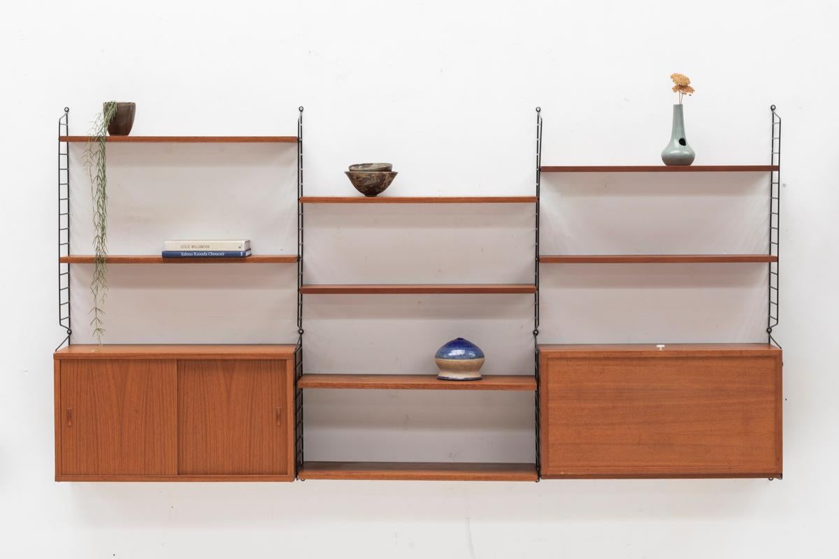Wall unit designed by Nisse Strinning and produced by String in Sweden around 1960. This modular wall unit contains two teak cabinets, one with sliding doors and one with a compartment for vinyl records. 8 Shelves rest on a black string rack. The