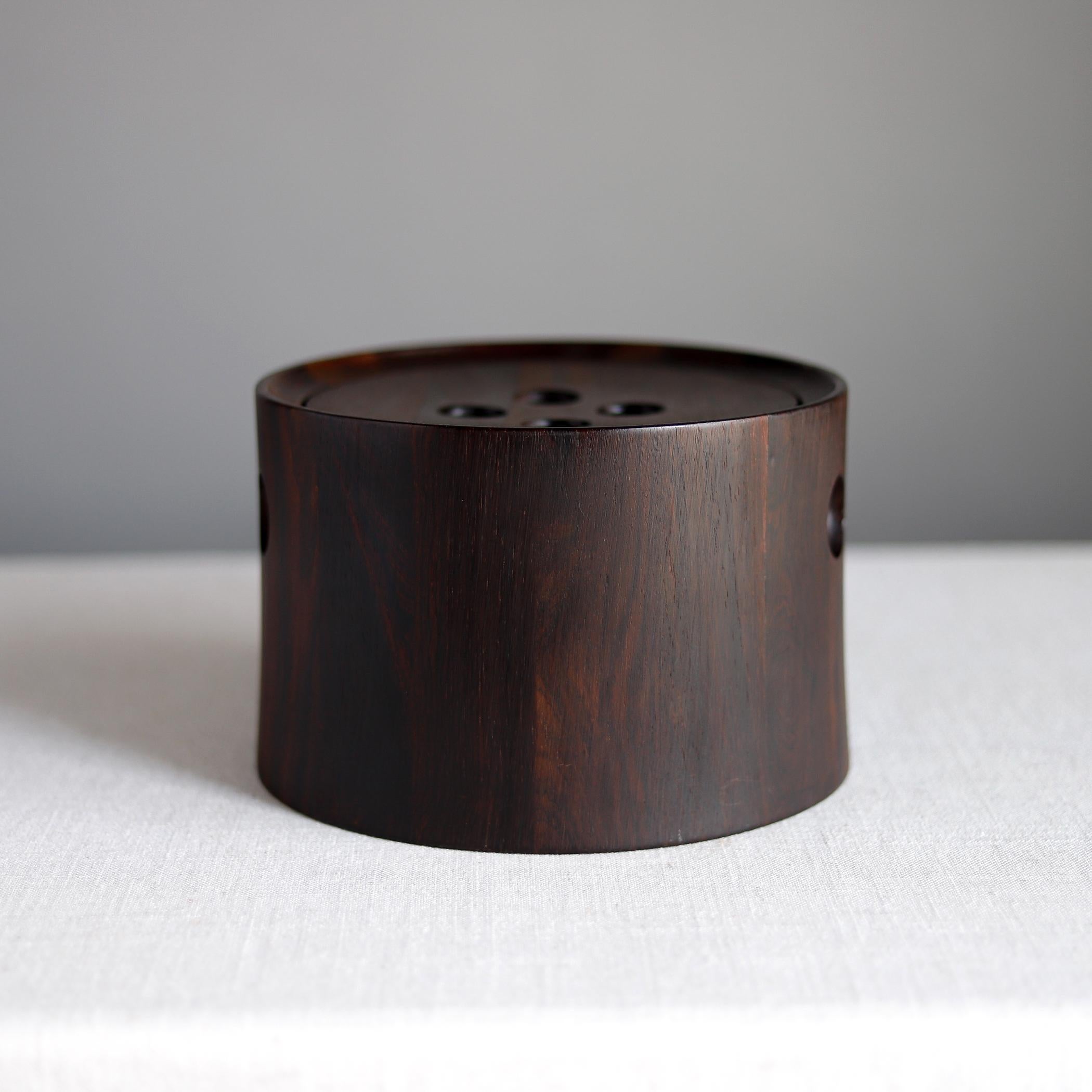 Staved rosewood ice bucket was made by Nissen. The lid and sides have recessed circles that serve as handles. The bucket retains its original black plastic liner and could be used for ice, or for keeping appetizers warm. 

Measures about 5 3/4