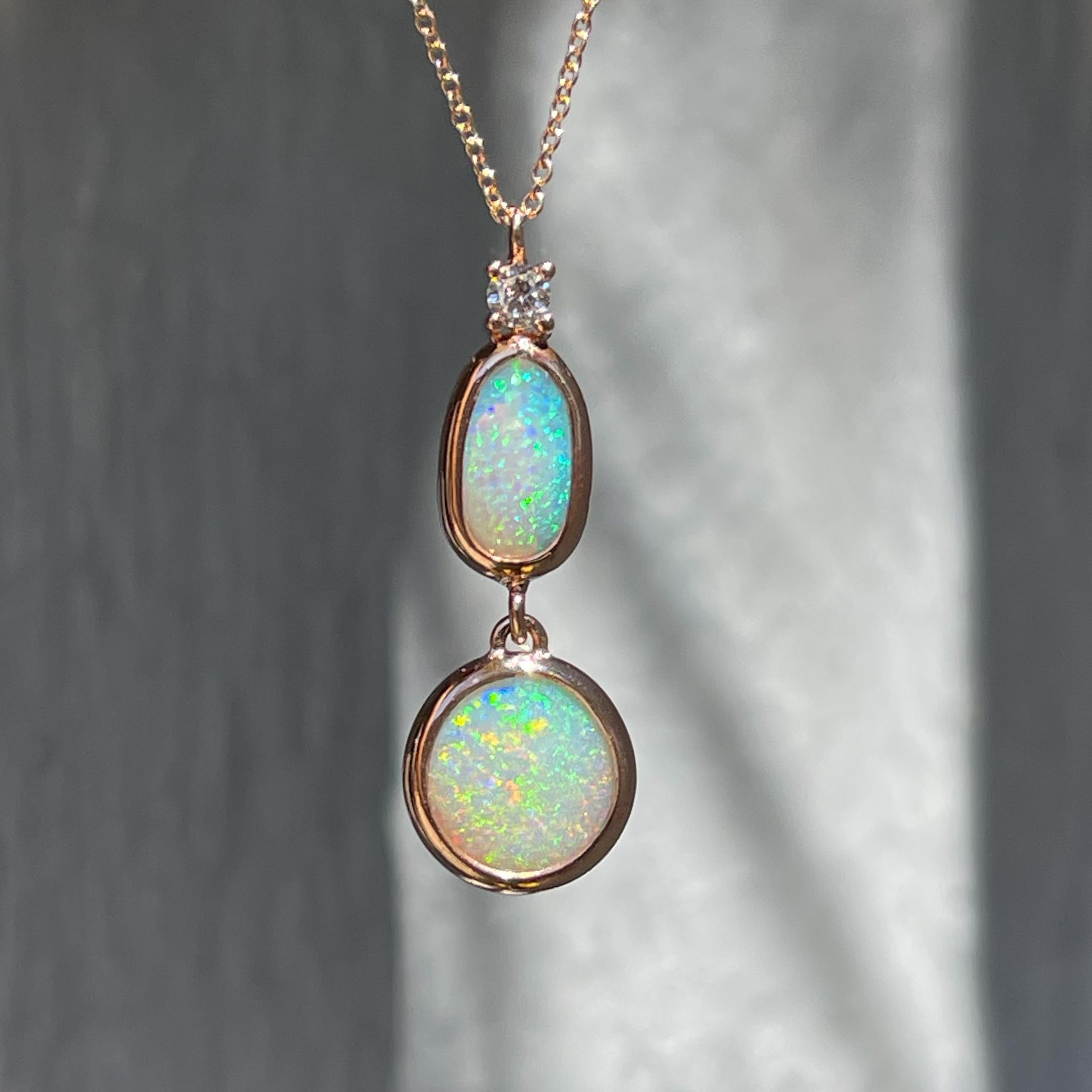 Les opales Lightning Ridge oscillent avec grâce dans ce collier d'opales australiennes. Serti d'un chaton en or rose, le pendentif en opale équilibre trois pierres visuellement pondérées. Un diamant étincelant est perché au sommet et s'articule