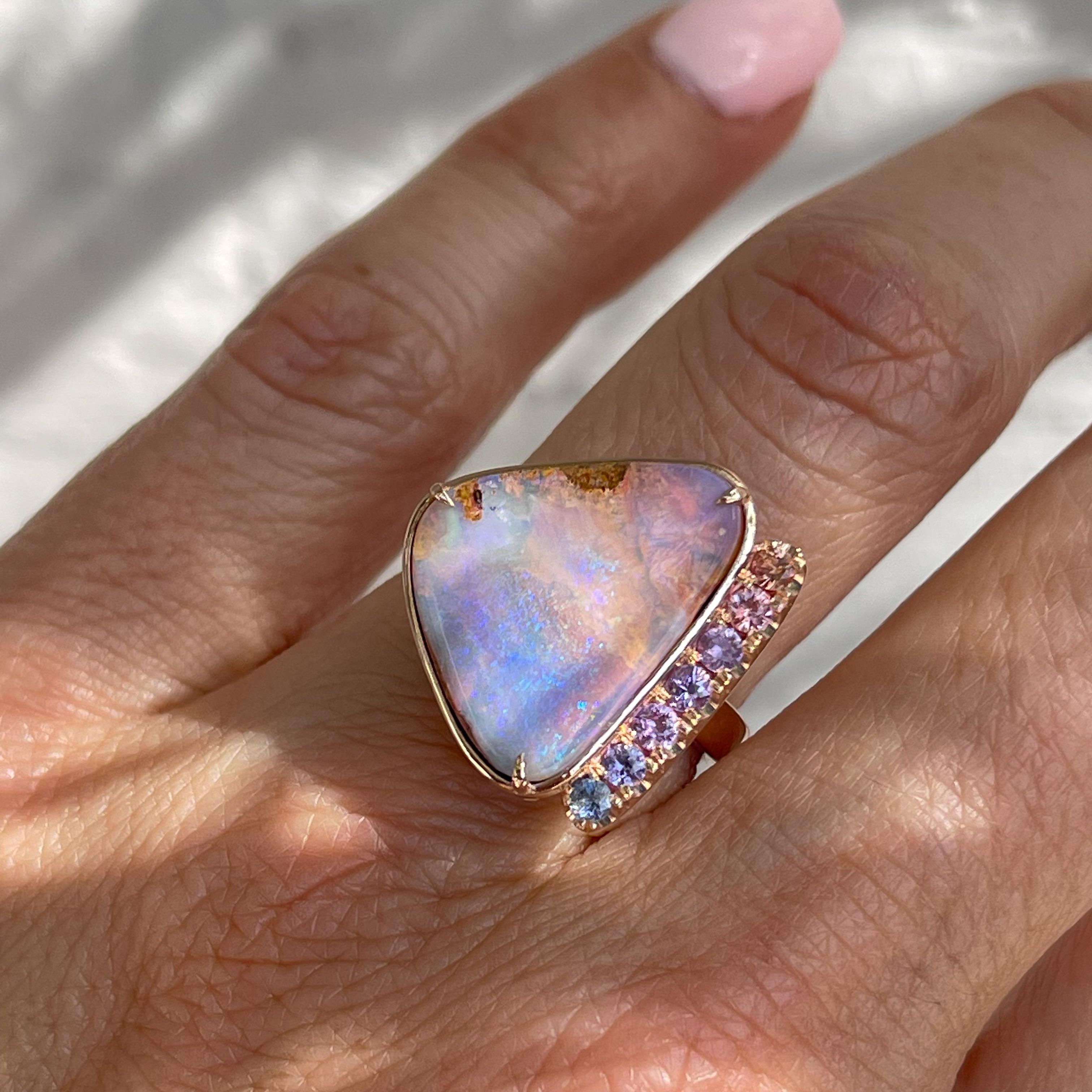 As sun sets, the skies perfuse with color in this Australian Opal Ring. From champagne pink to lavender and blue, the Boulder Opal casts stunning hues. A cascade of sapphires borders the stone in a striking chromatic complement. Though multi-toned,