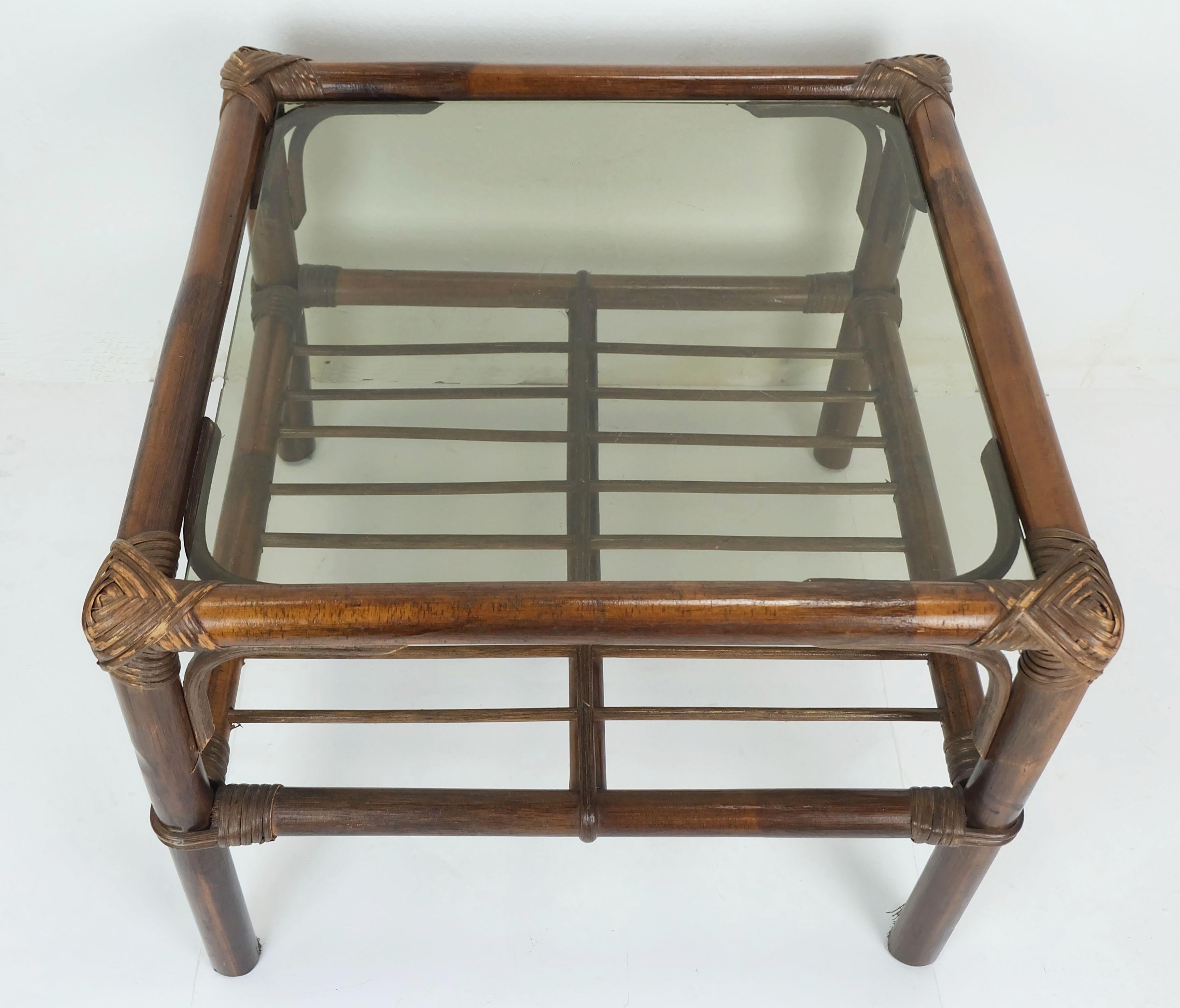 Très belle et décorative table d'appoint / table basse des années 1970. Fabriqué en bambou et osier teinté foncé avec un plateau en verre fumé.

Dimensions en cm :
Largeur 51 cm, profondeur 51 cm, hauteur 40 cm. Le plateau en verre mesure 43 x 43