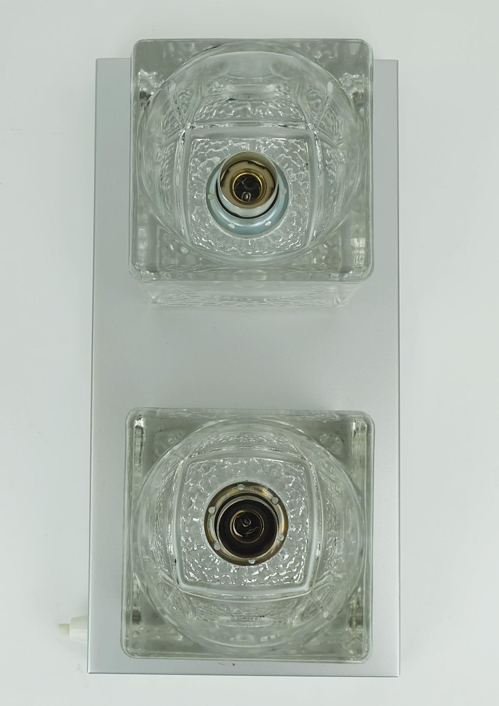 Una bellissima applique degli anni '60-'70 di Peill & Putzler, modello No. 71056. La base è in ottone con finitura laccata argento opaco. 2 paralumi a forma di cubo in vetro trasparente spesso. Per lampadine E14. Il suo aspetto migliore si ottiene