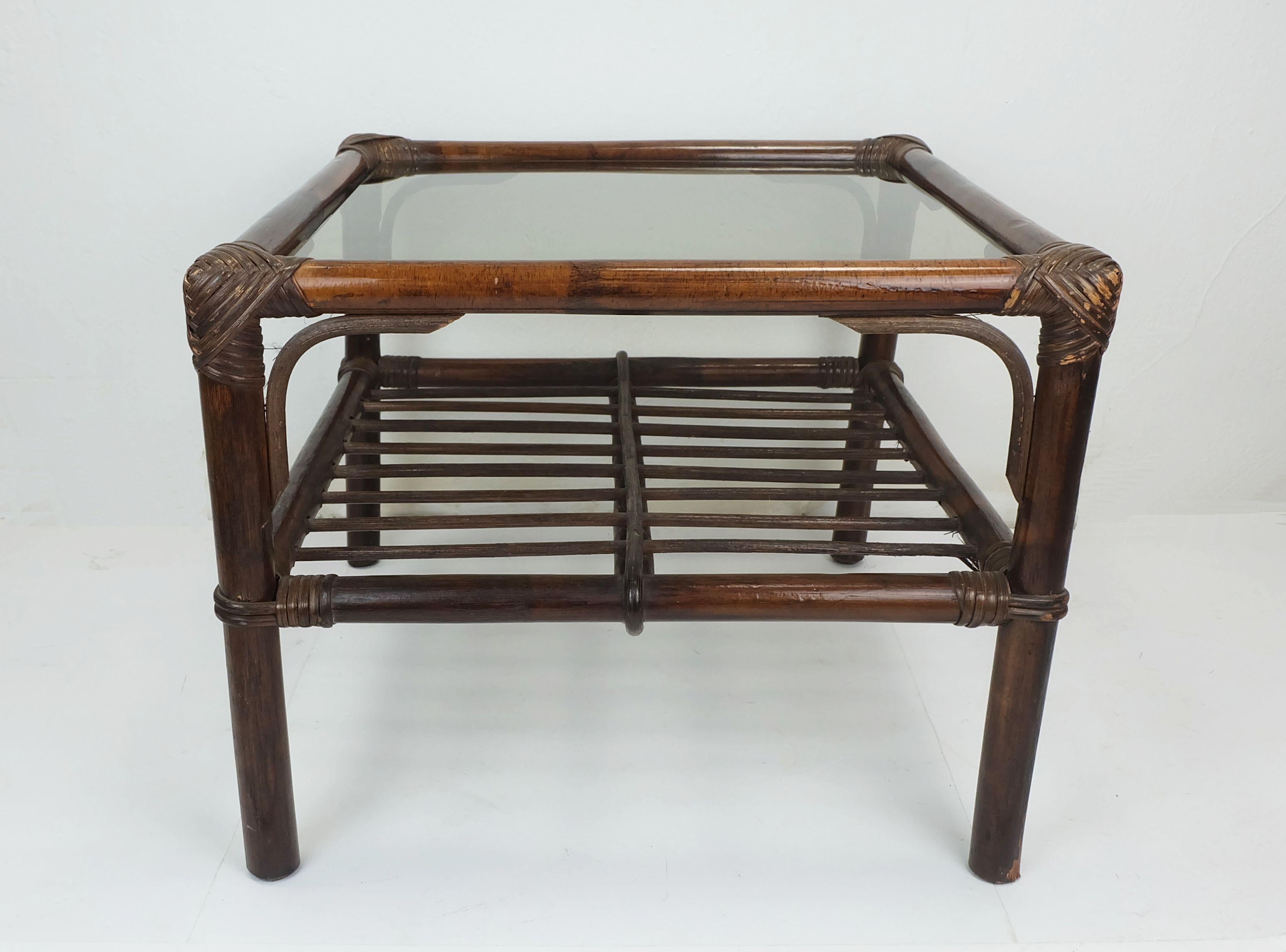 Très belle et décorative table d'appoint / table basse des années 1970. Fabriqué en bambou et osier teinté foncé avec un plateau en verre fumé.

Dimensions en cm :
Largeur 51 cm, profondeur 51 cm, hauteur 40 cm. Le plateau en verre mesure 43 x 43