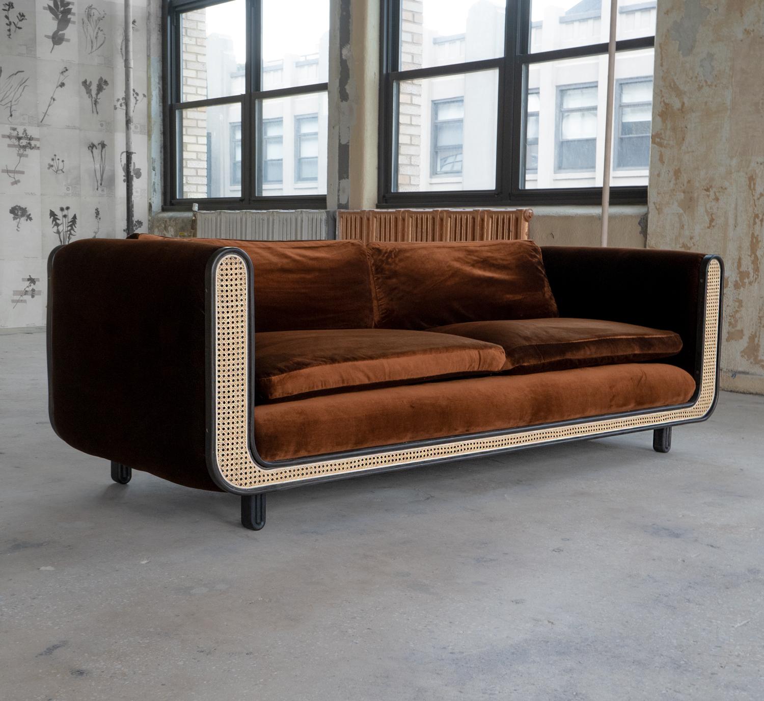 The Nº105 couch is composed of a natural cane sofa back, seat back and face which allows air and pass through the seat back and arms. Steam-bent ebonized ash trim wraps the front and back profile. Cushions are made from foam and down fill. Sofa