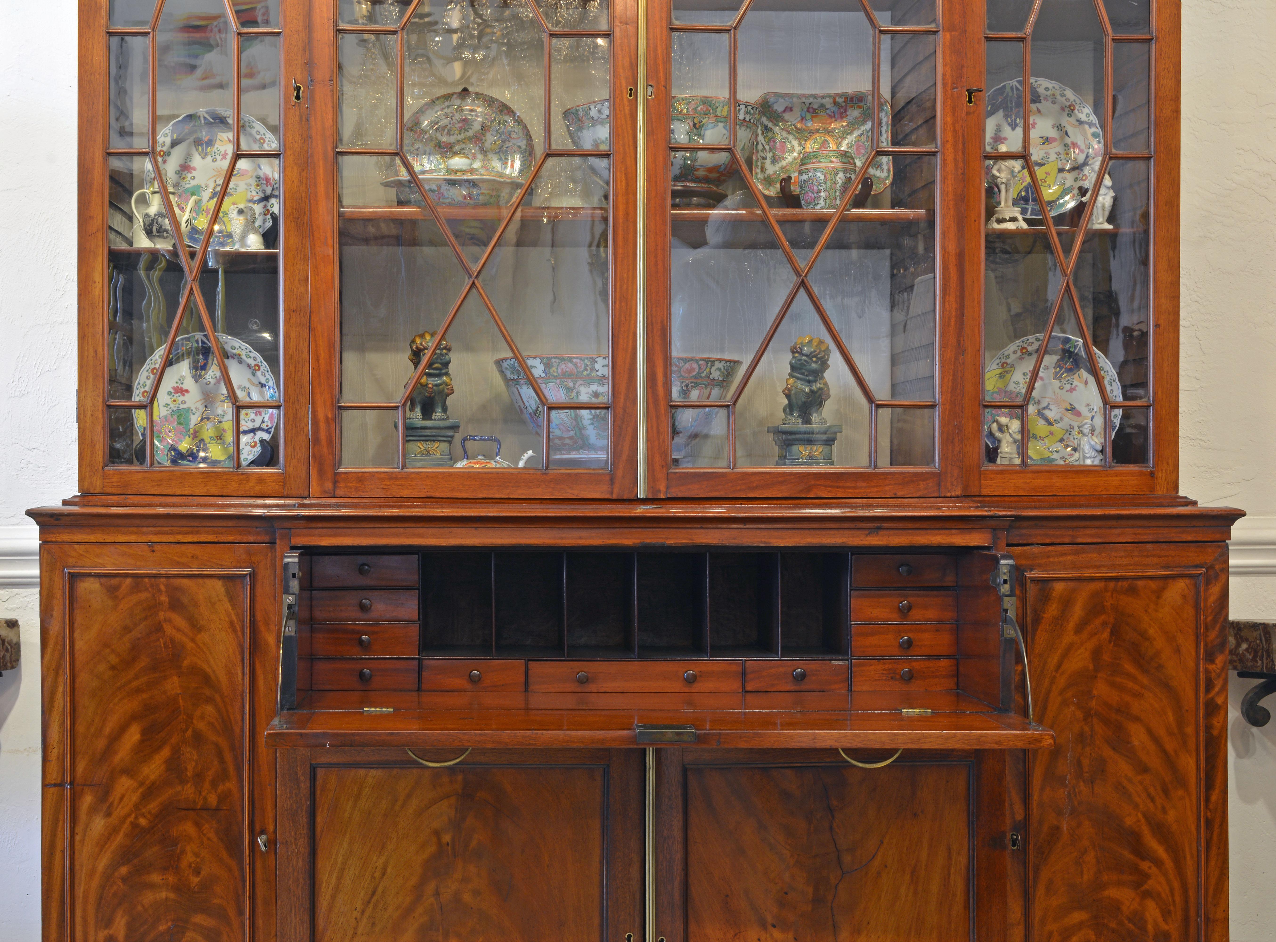 This stately secretary bookcase of great proportions features a central drawer which upon pull out opens up to an interior fitted with smaller drawers and open compartments above a mahogany writing surface. The four glazed doors of the upper section