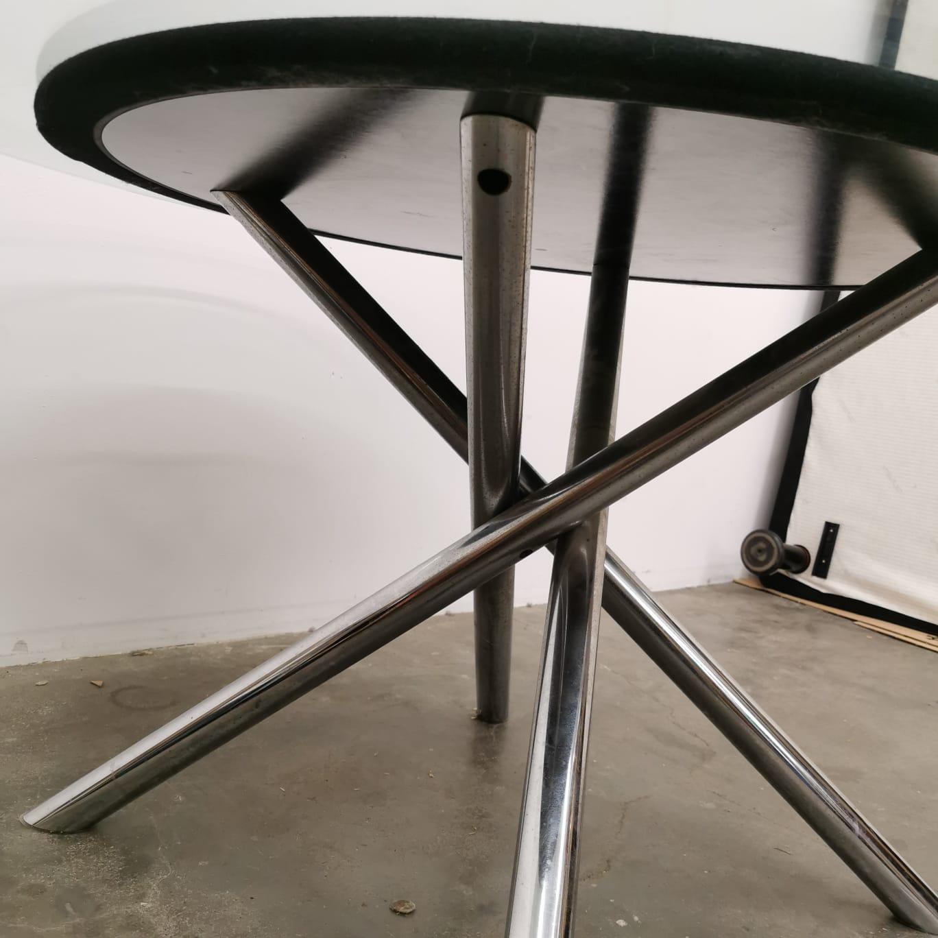 Une table de style post-moderne en acier et verre, composée d'un élément central inférieur qui exprime une forte tension formelle et d'un plateau en verre simple avec un élément central noir.