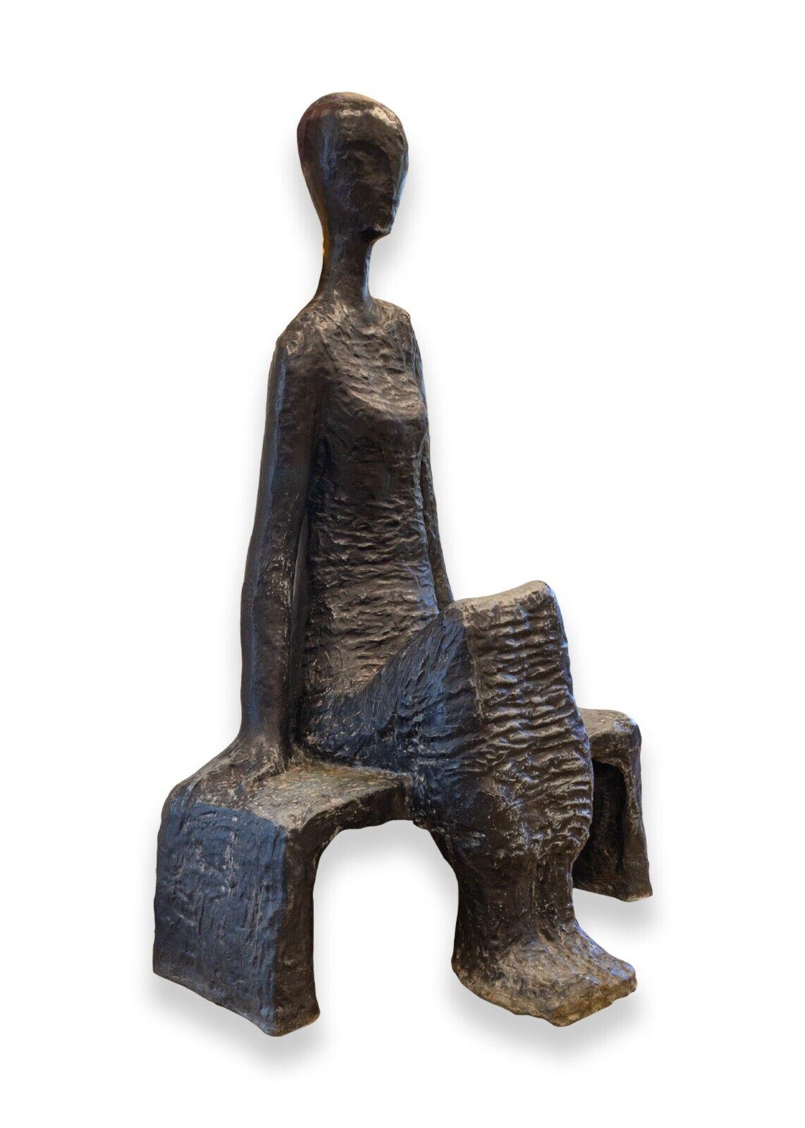 A minimalist modernist bronze sculpture depicting an abstract seated figure by German Israeli artist Noemi Schindler. Circa mid-20th century. The composition is elegant with a brutalist quality and the figure evokes a meditative or Zen emotion. This