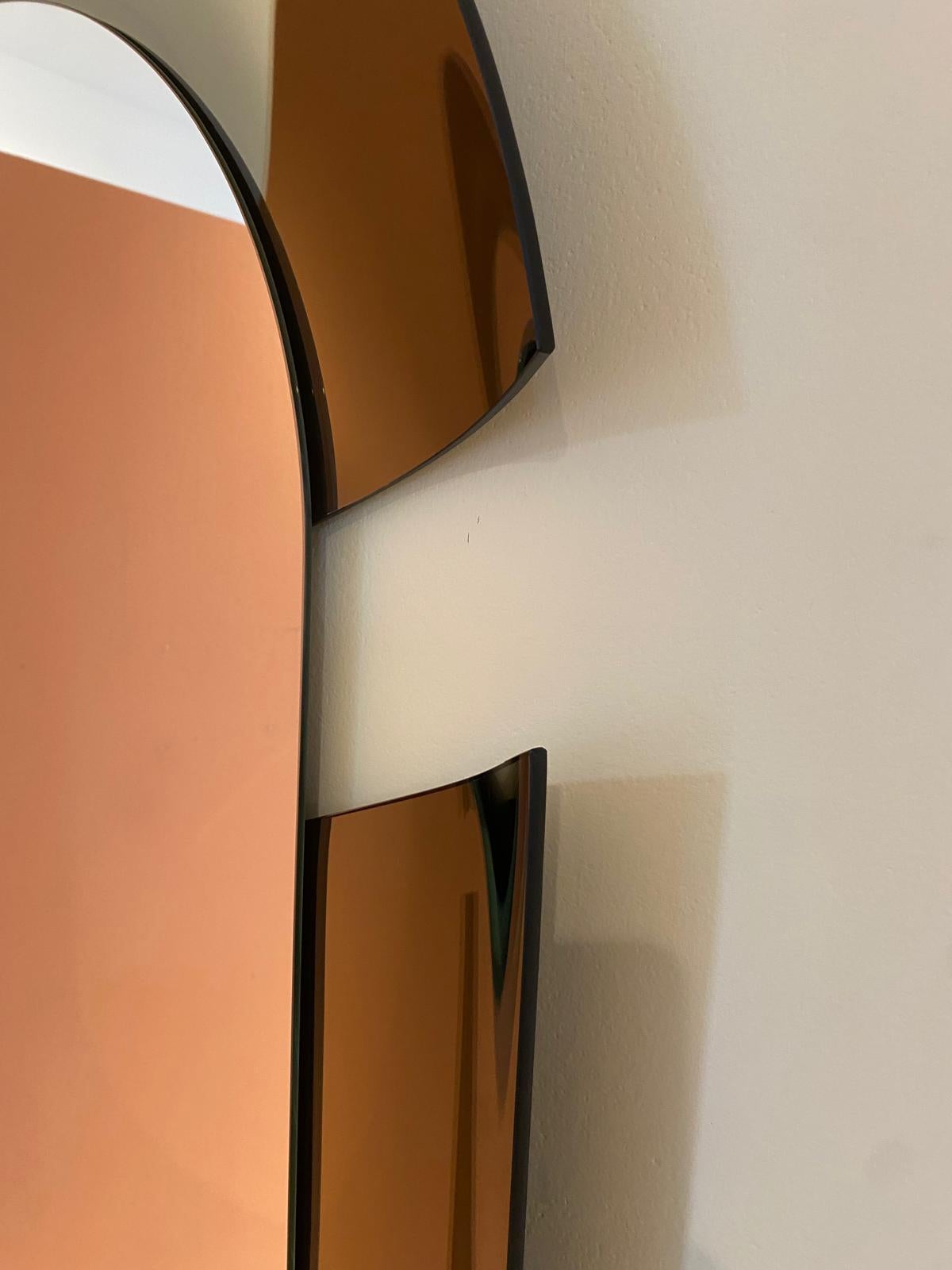 Contorno longilineo ed ellittico, viene interrotto da un taglio netto che risalta un effetto dinamico e ricercato.

Specchio composto da due elementi. Specchiera centrale in vetro piano, cornice specchiata e curvata concava.